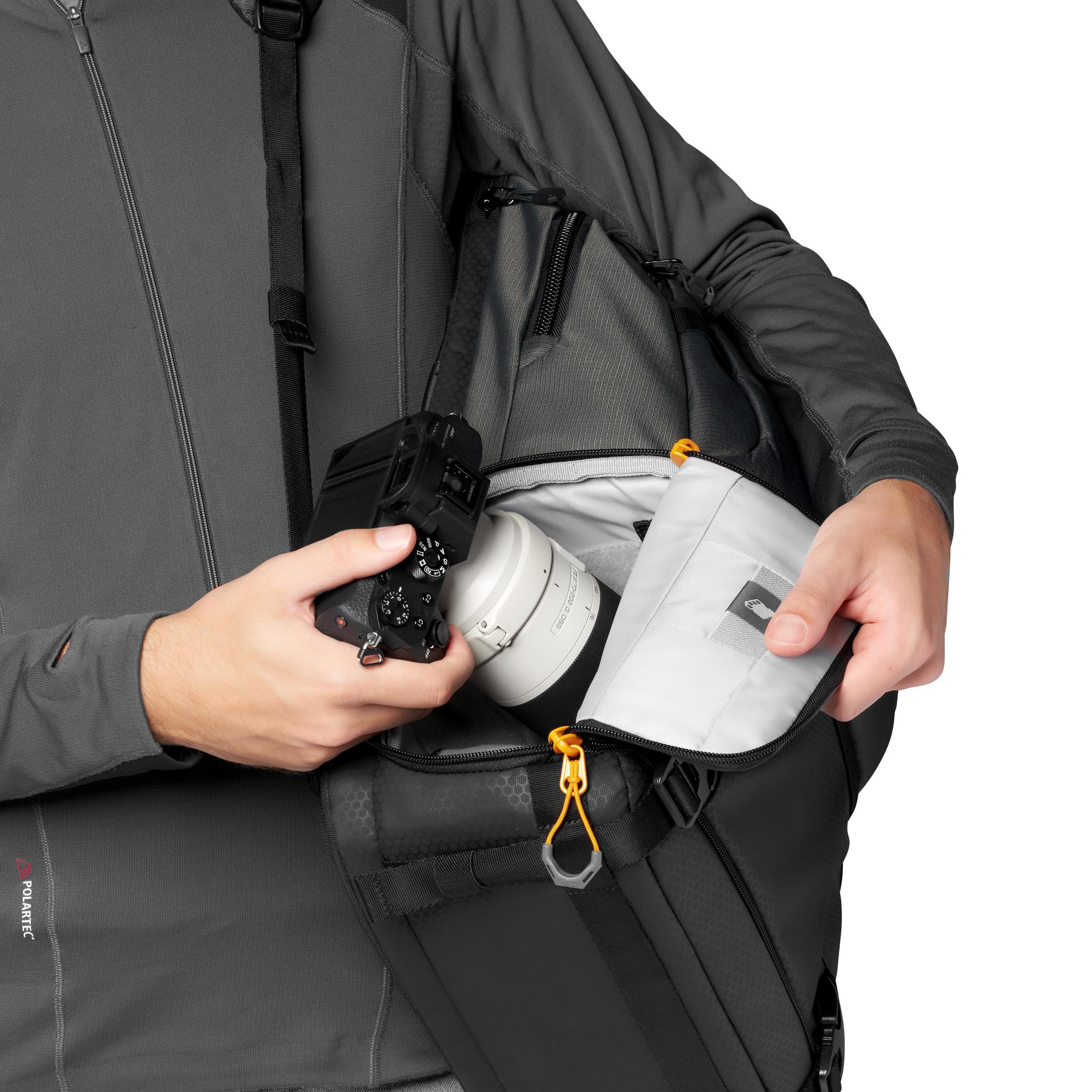 Une personne ouvrant un sac d'appareil photo révélant un appareil photo et un objectif. Sac noir avec des accents orange.