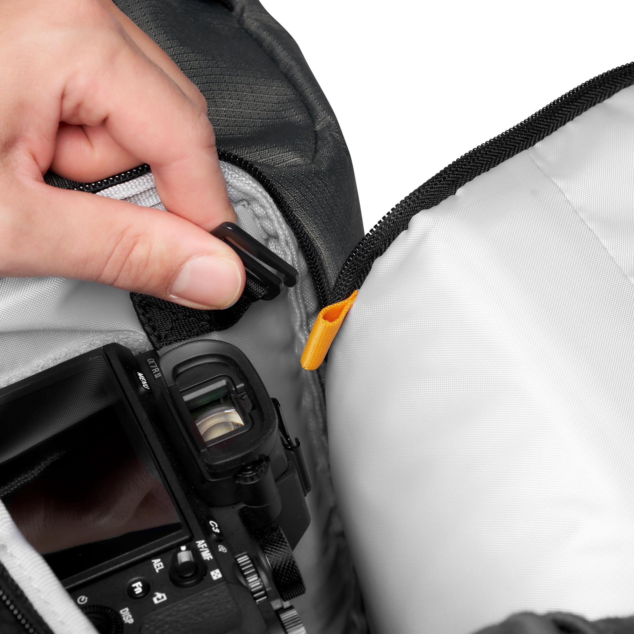 Main ouvrant un sac photo, révélant un appareil photo. Le sac a un intérieur blanc.