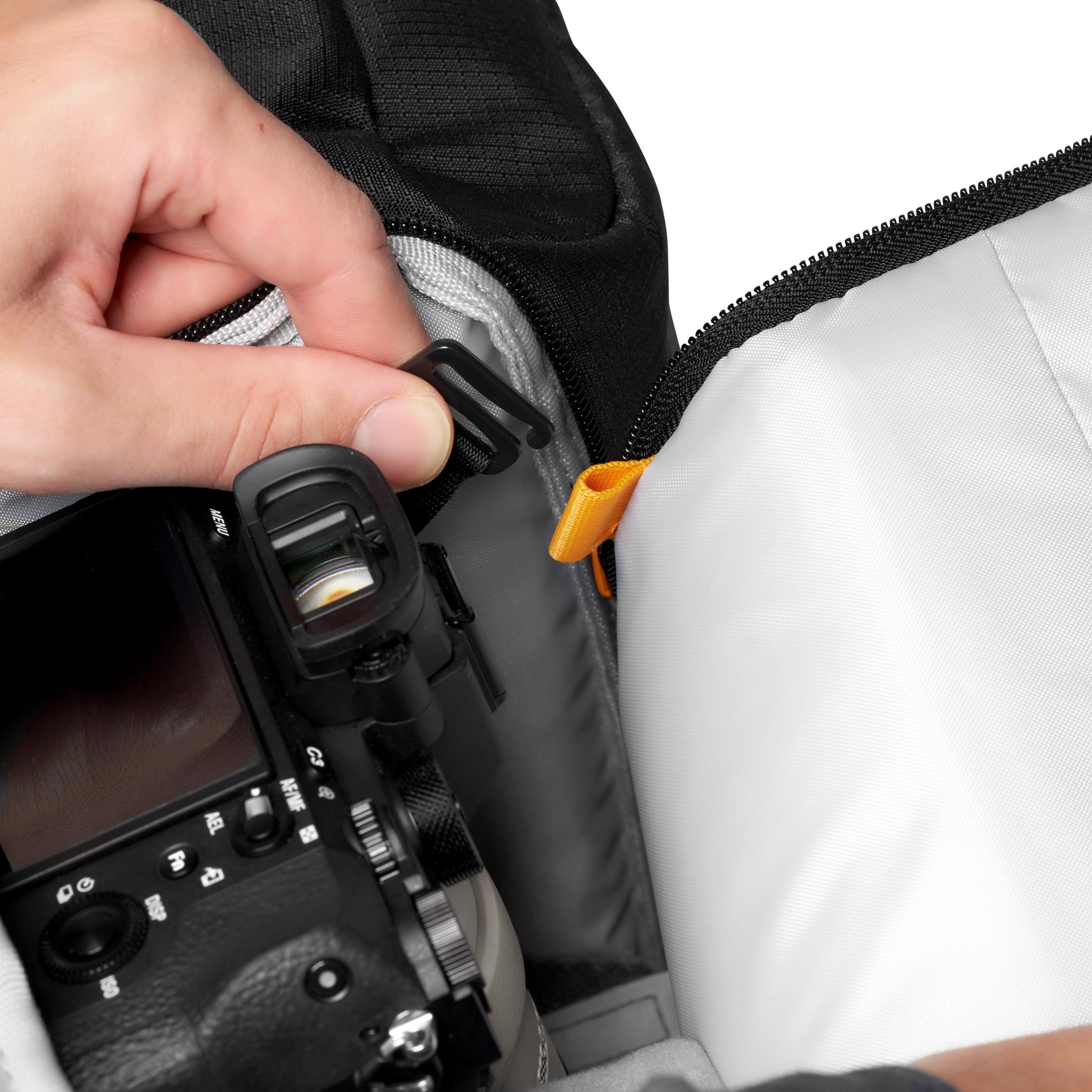 Une main fixe une sangle noire dans un sac photo noir.