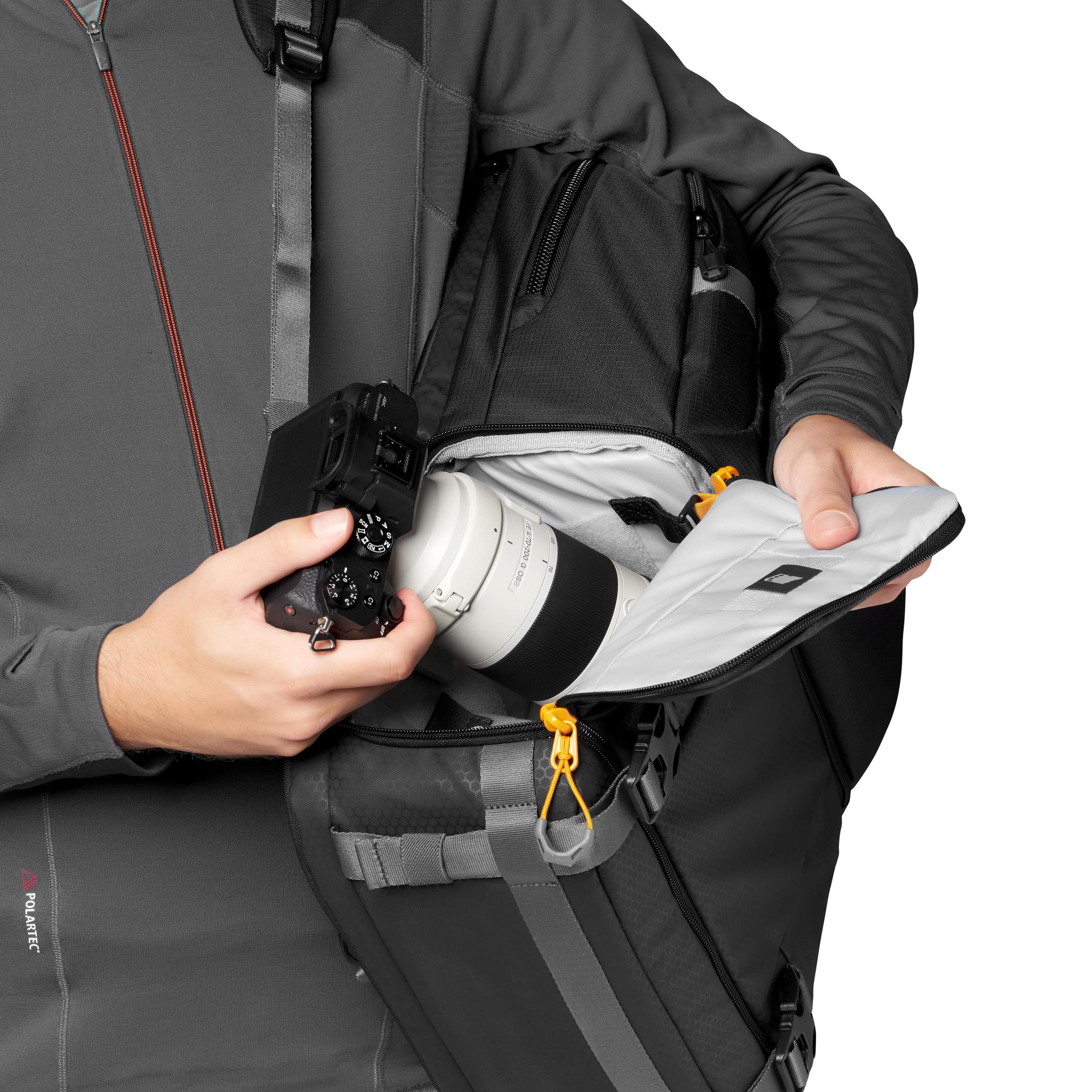 Une personne tient un appareil photo et un objectif d'un sac à dos. Fond blanc.