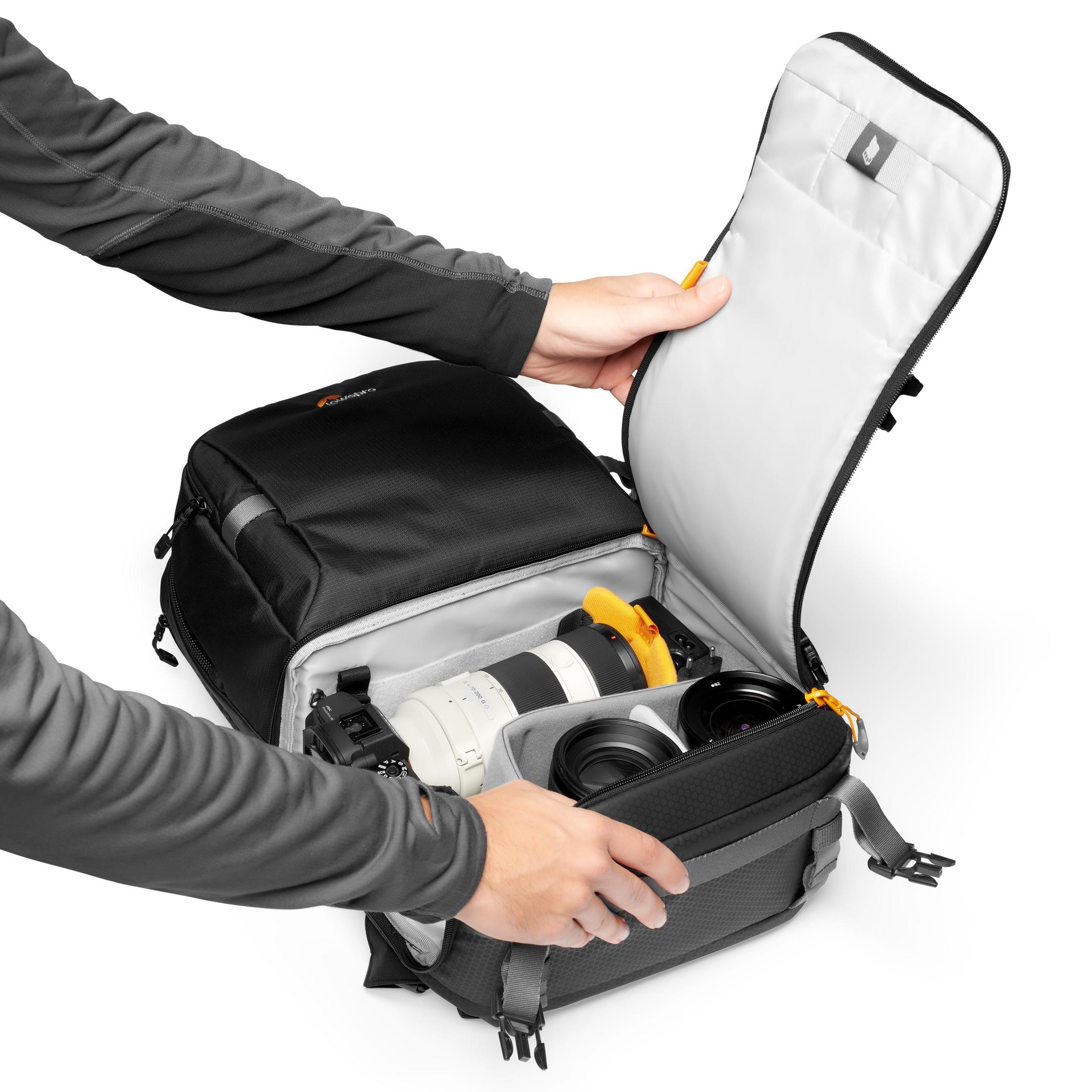 Mains ouvrant un sac photo noir. Appareil photo et objectifs à l'intérieur. Fond blanc.