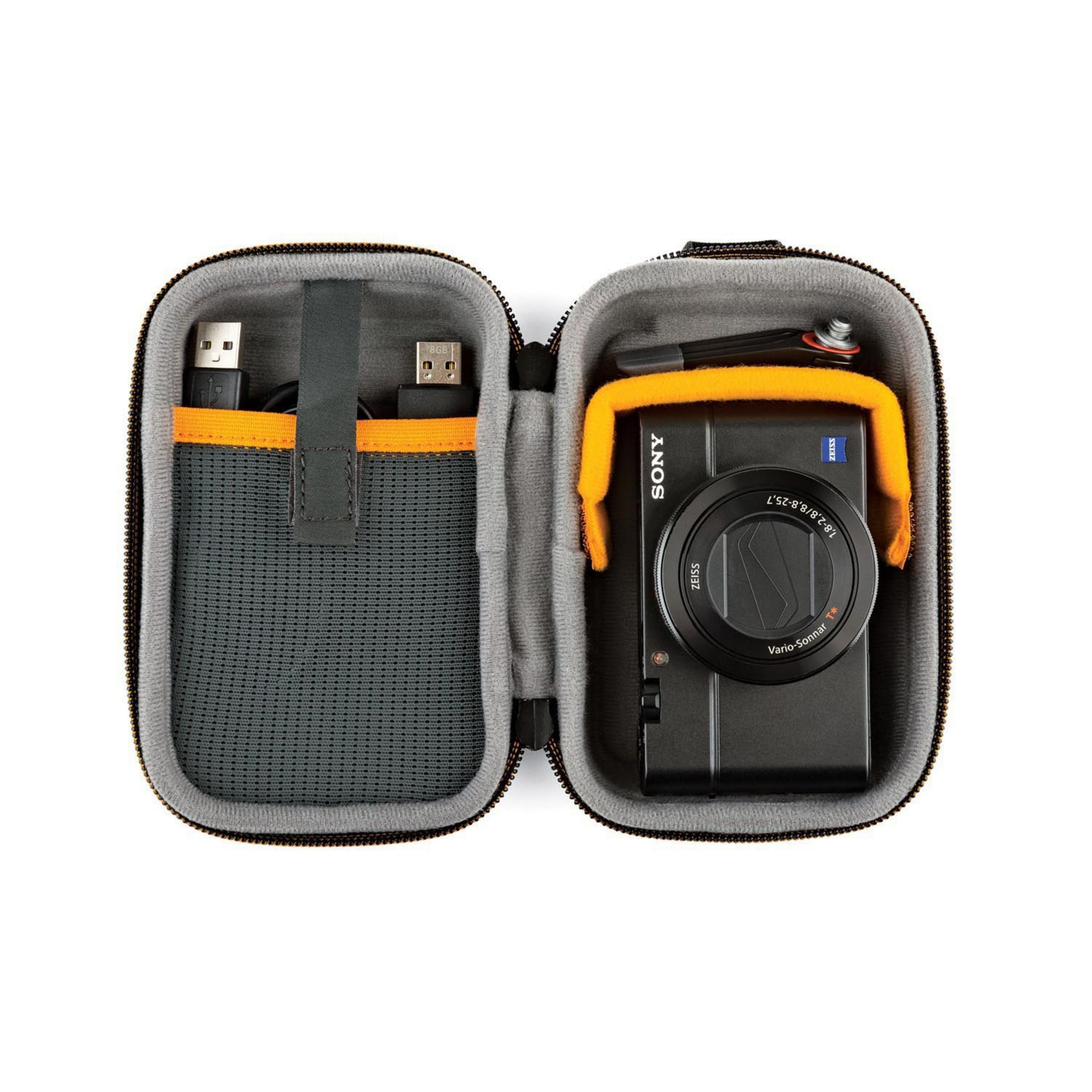 Custodia per fotocamera aperta con fotocamera, cavo e caricabatterie all'interno, su superficie bianca.