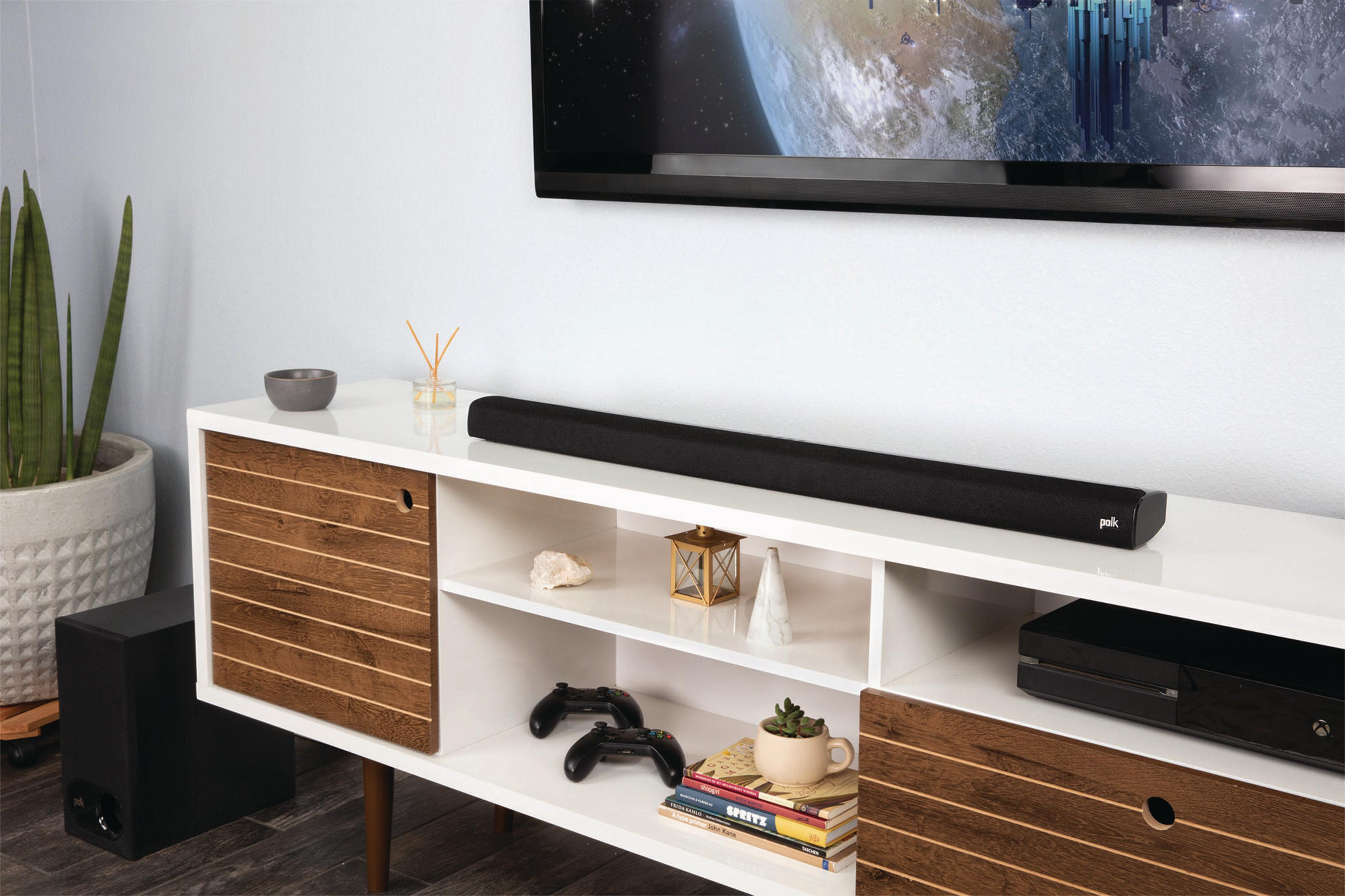Eine Soundbar auf einem weißen Schrank unter einem Fernseher. Ein schwarzer Subwoofer steht auf dem Boden.