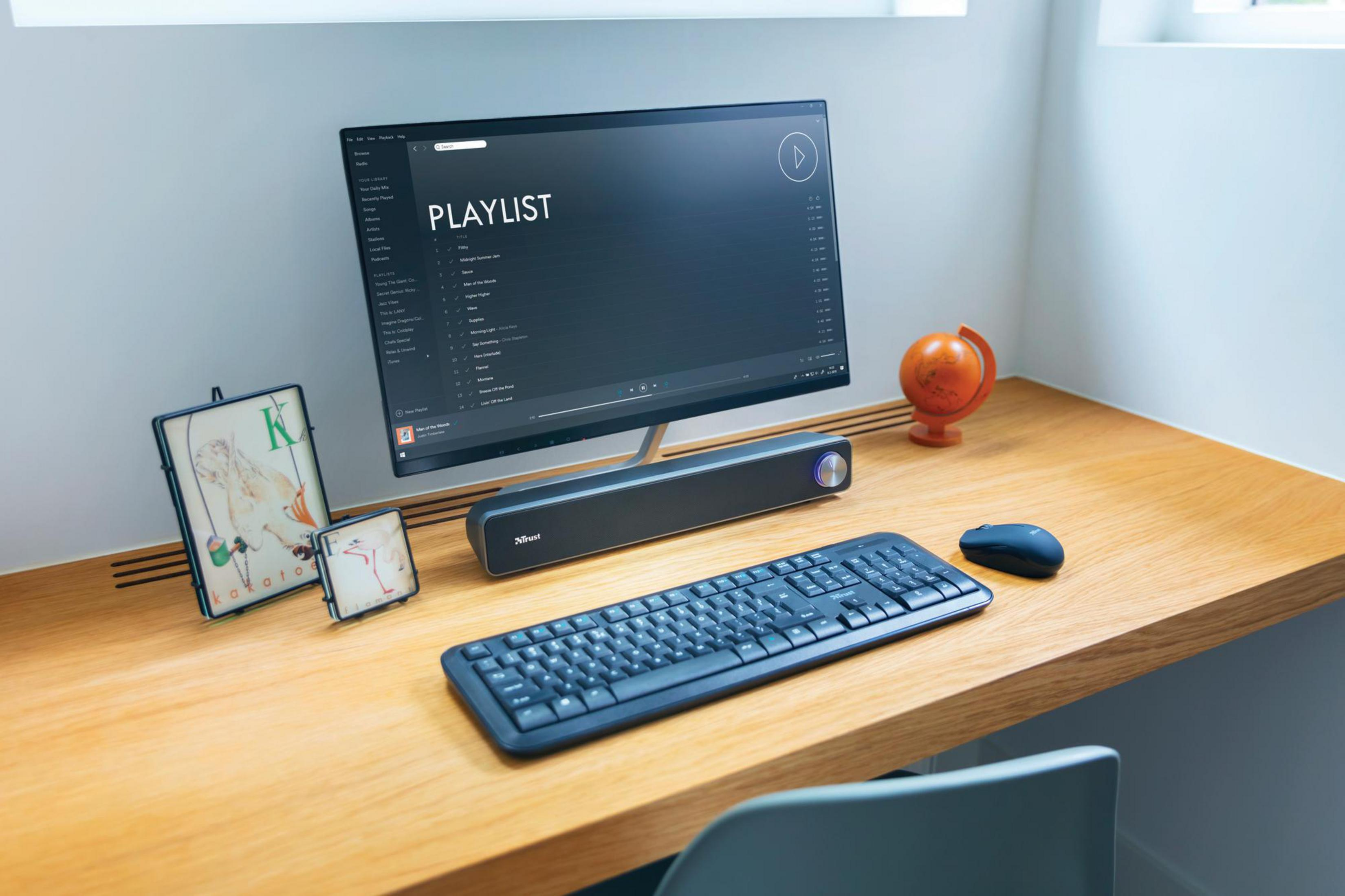 Biurko z monitorem, klawiaturą, myszką, głośnikiem i elementami dekoracyjnymi.