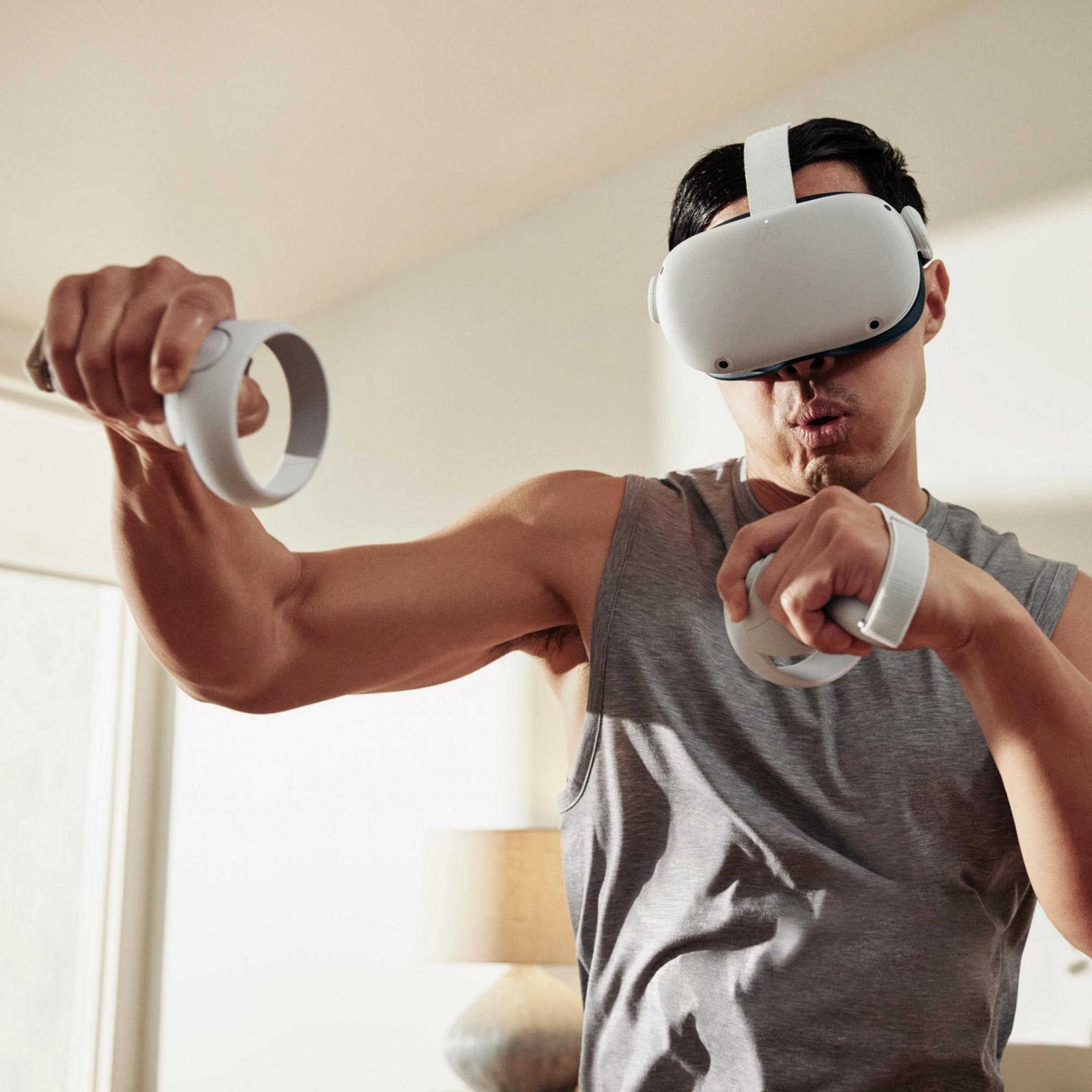 Un hombre usando un visor de realidad virtual y sosteniendo controladores. Está en una habitación con una lámpara y una pared clara.