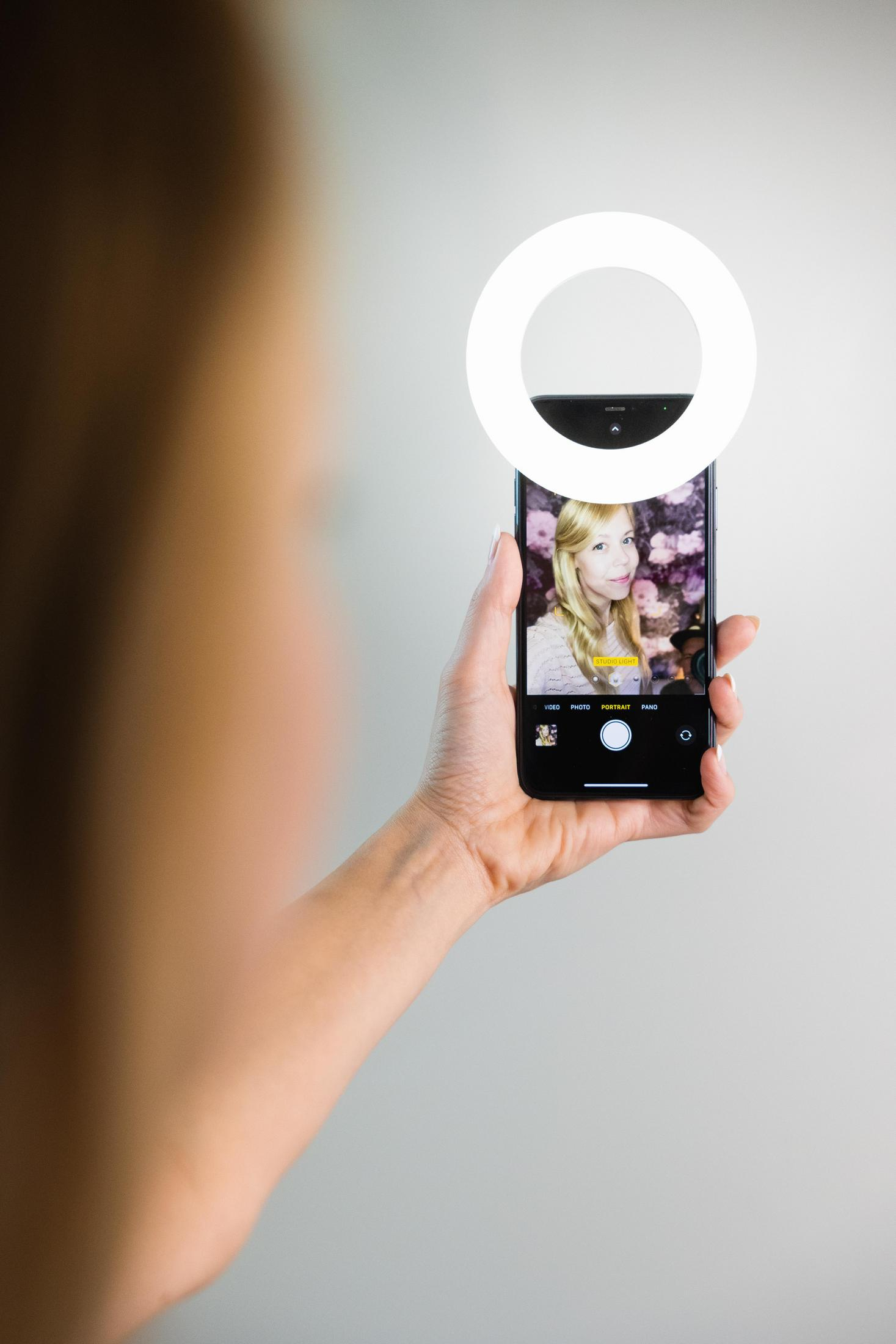 Eine Frau hält ein Telefon mit Ringlicht und macht ein Selfie.