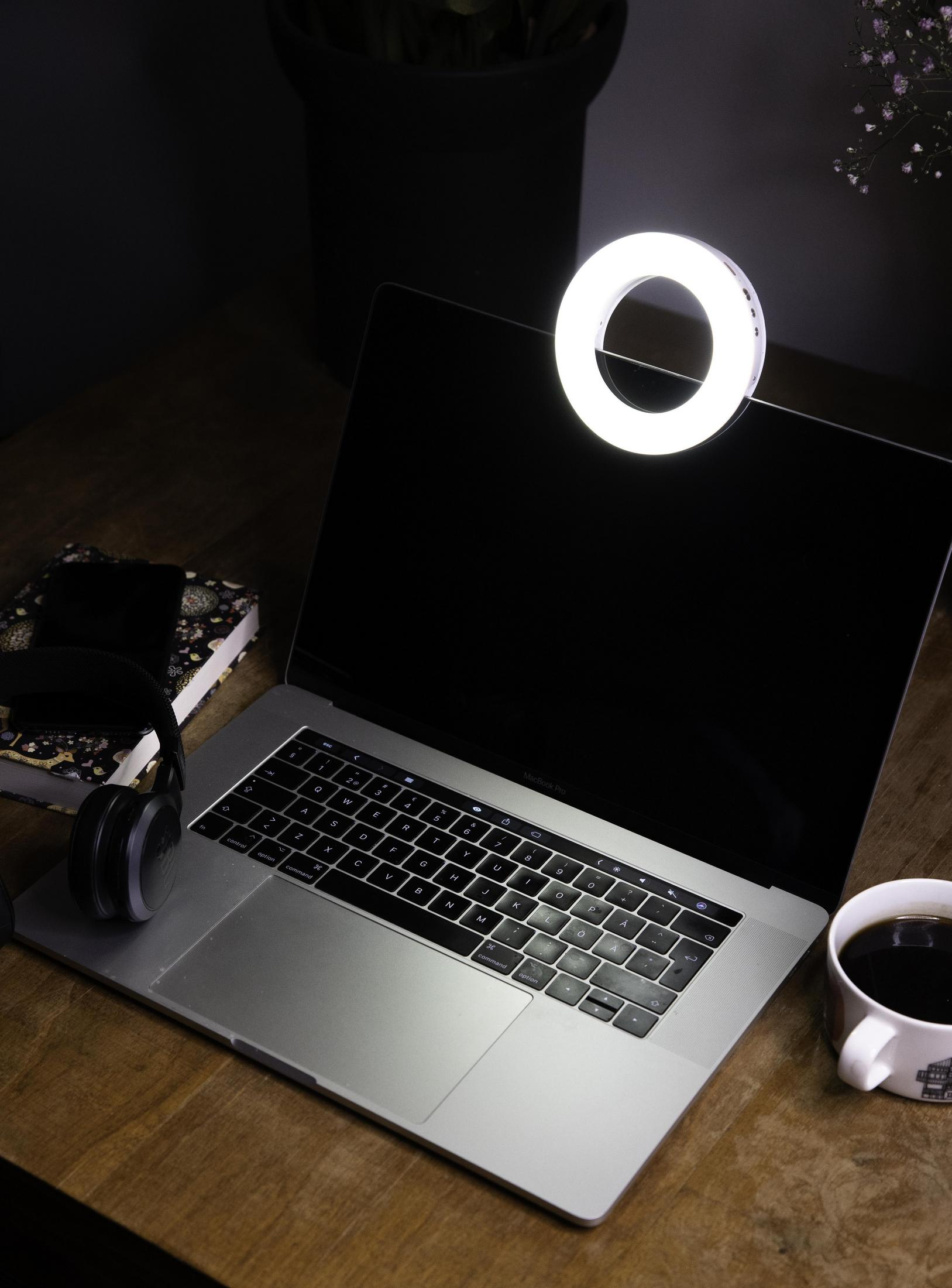 Ein Laptop mit Ringlicht auf einem Holztisch mit einer Kaffeetasse und einem Notizbuch.