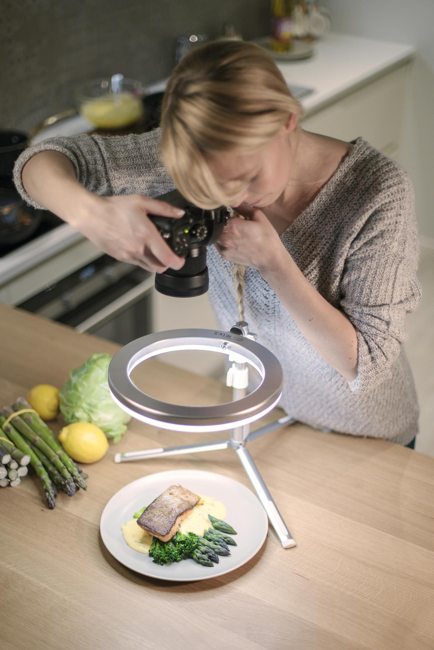 Frau fotografiert Essen mit Kamera und Ringlicht. Es gibt Zitronen und Spargel.