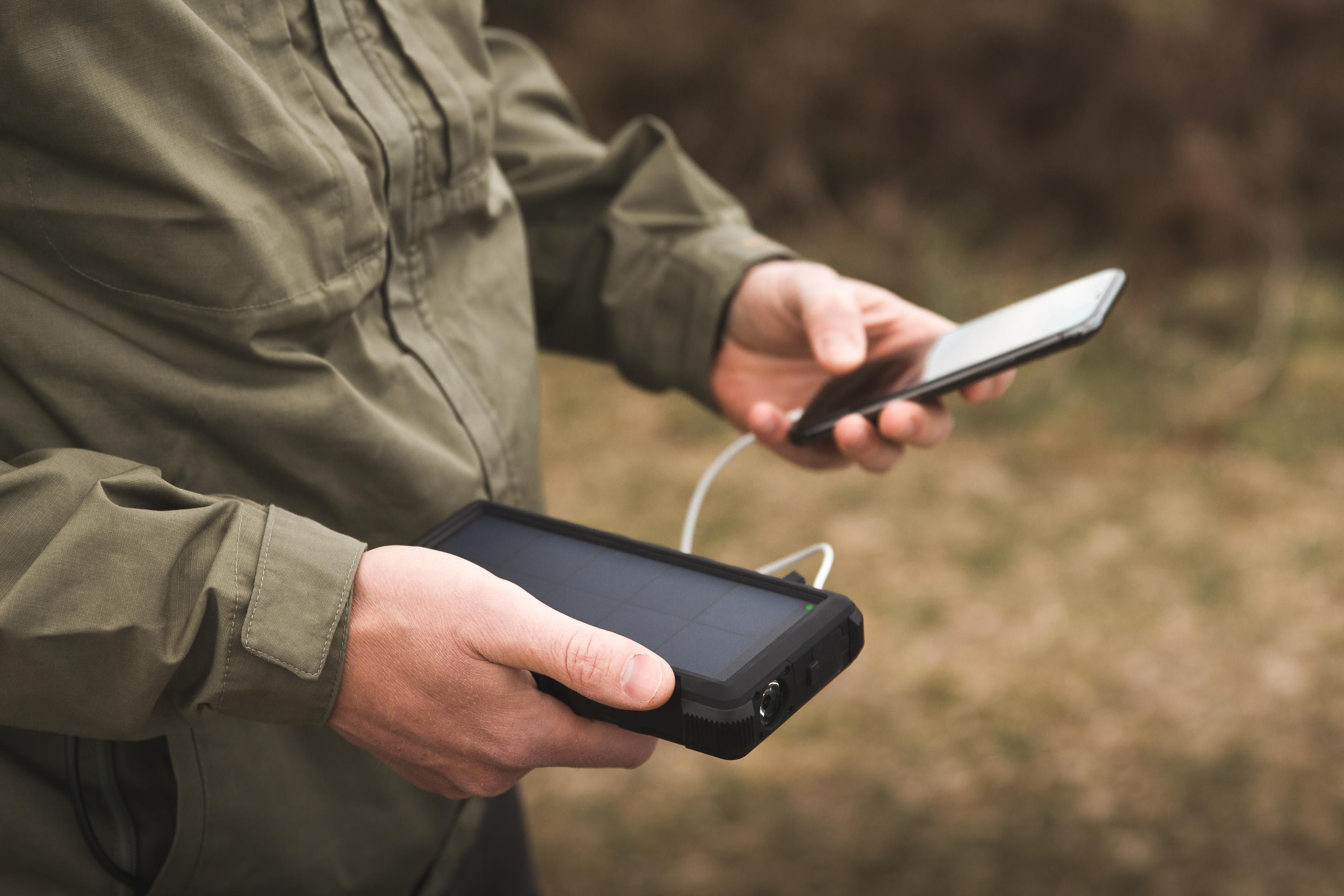 Persona che tiene un caricatore solare e uno smartphone in un ambiente naturale.