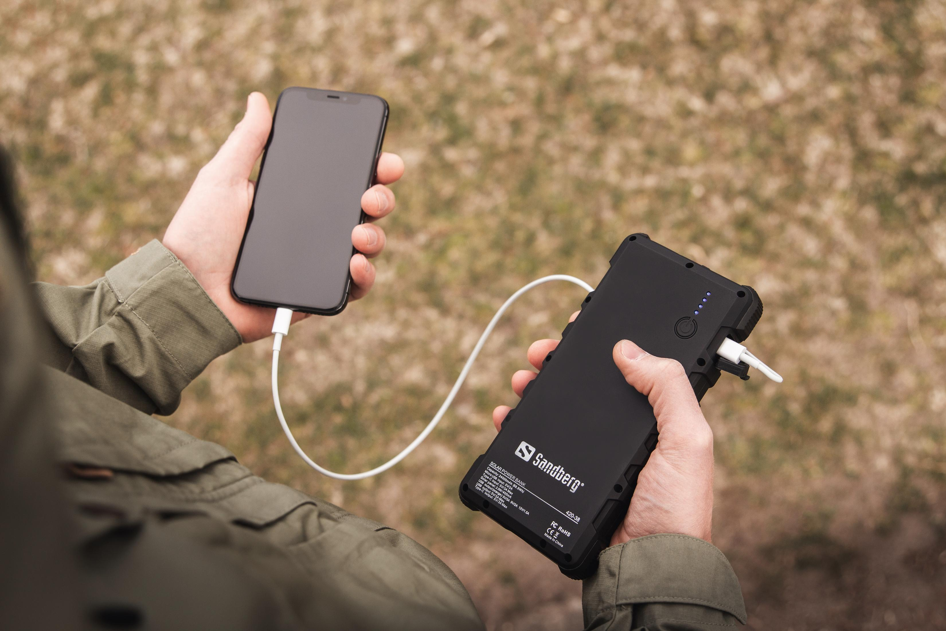Una persona tiene in mano uno smartphone e un power bank nero con cavo bianco.
