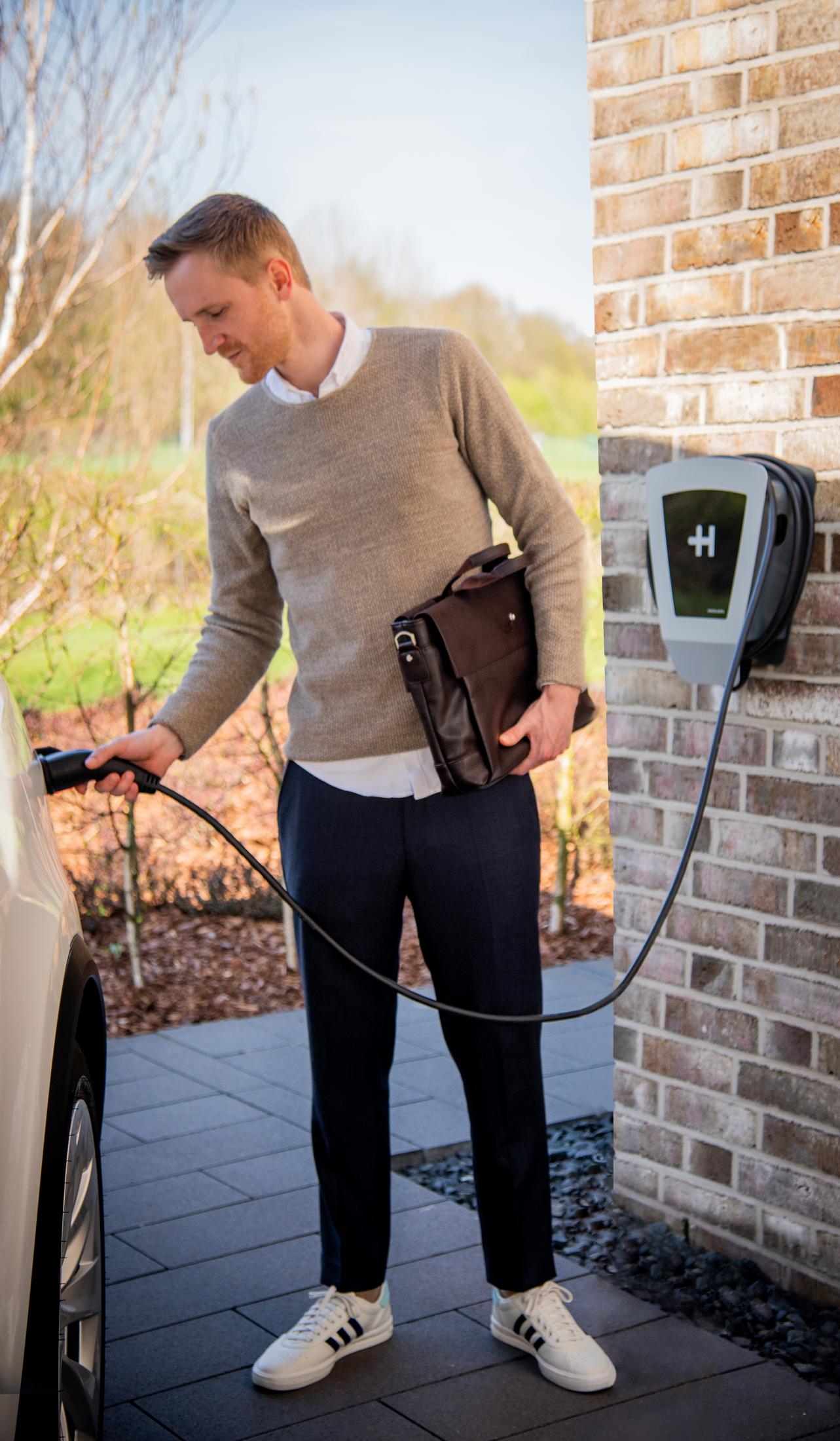 Un homme charge une voiture électrique avec une borne de recharge en arrière-plan.