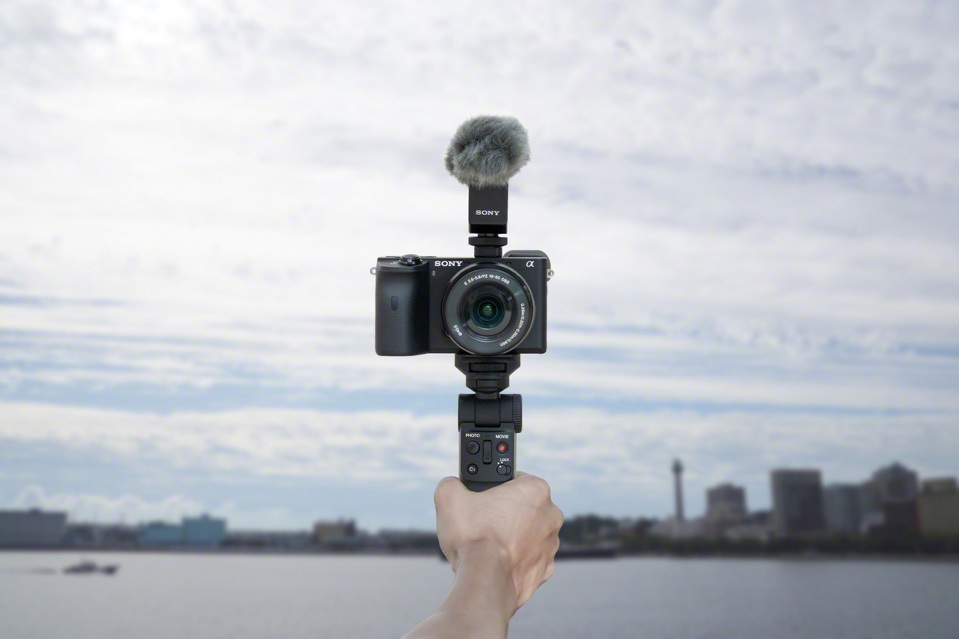 Una mano sostiene una cámara y un micrófono negros de Sony contra un horizonte con agua y edificios.