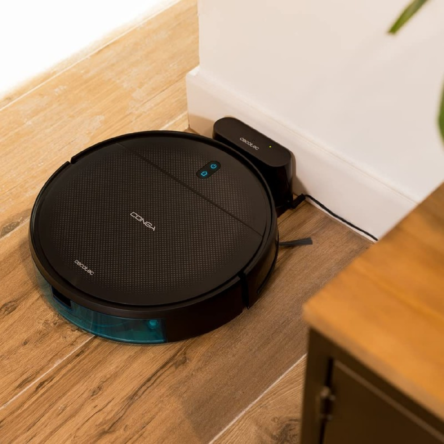 Una aspiradora robot negra en un piso de madera junto a su estación de carga y un armario.