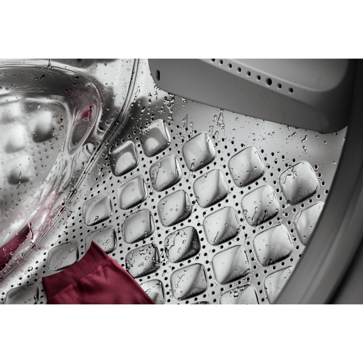 Wnętrze bębna pralki, stal nierdzewna, z mokrym czerwonym materiałem.