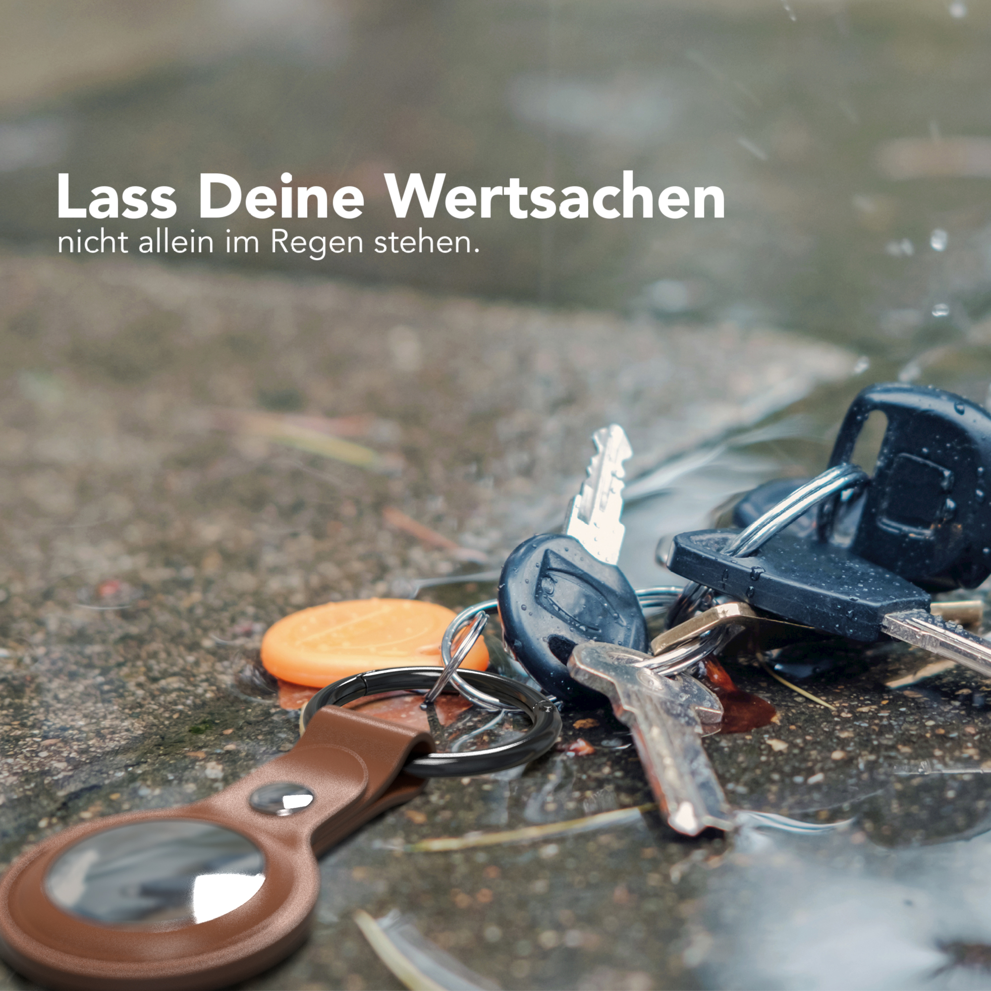 Schlüssel und Anhänger auf nassem Untergrund. Der Hintergrund zeigt Regen.