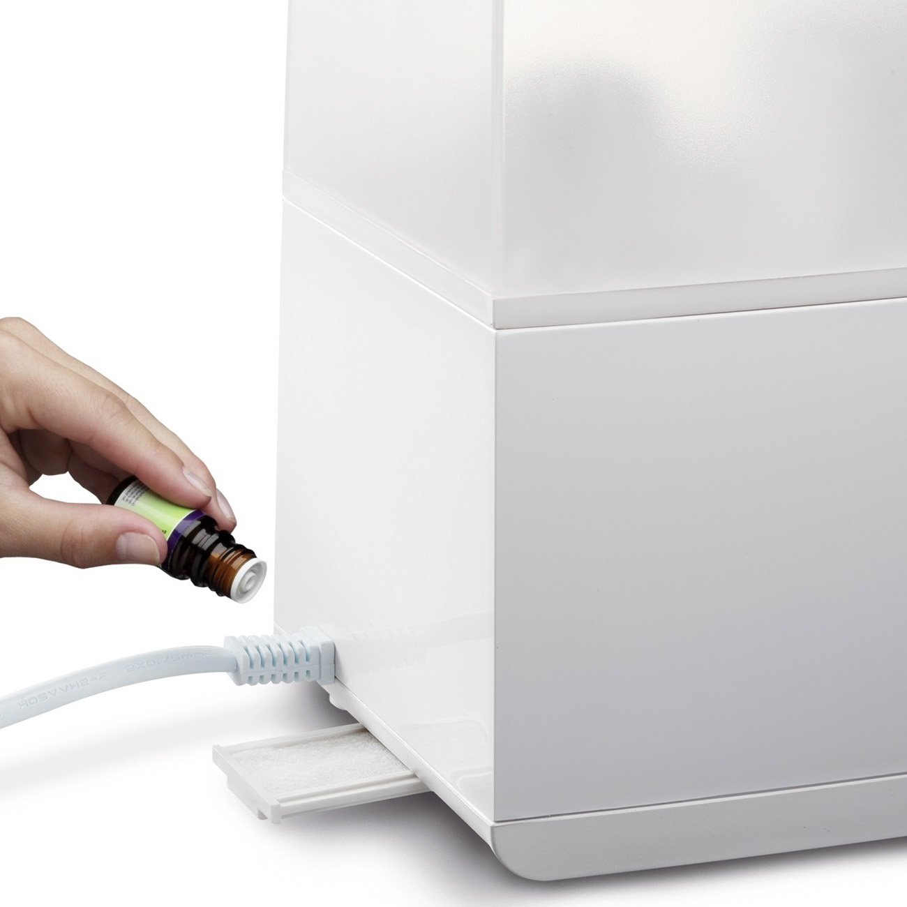 Mano versa liquido da una piccola bottiglia in un dispositivo bianco per aromaterapia, primo piano.