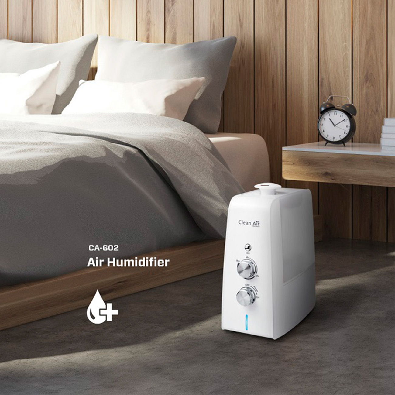 Umidificatore d'aria bianco sul pavimento vicino a un letto. Ha due manopole e il marchio 'Clean Air'.