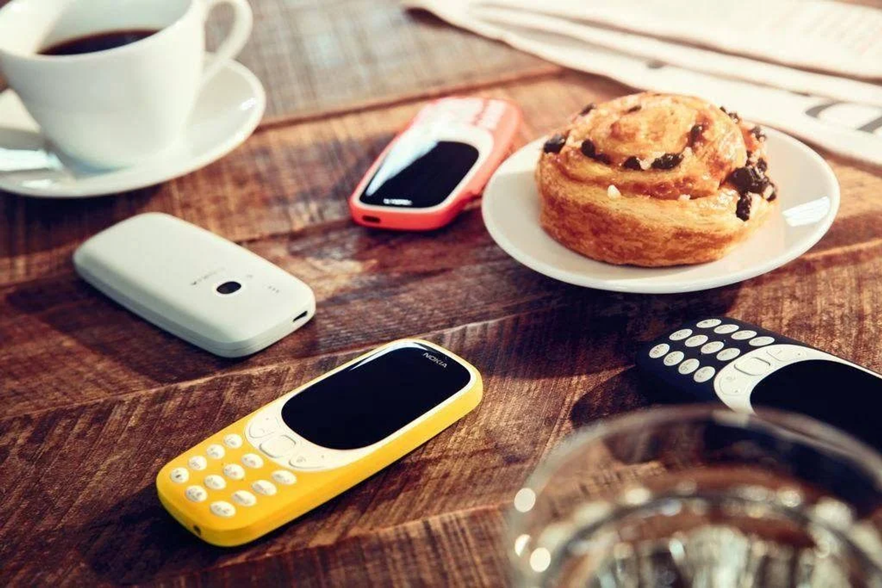 Telefony, filiżanka kawy i ciastko na drewnianym stole. Różne kolory.