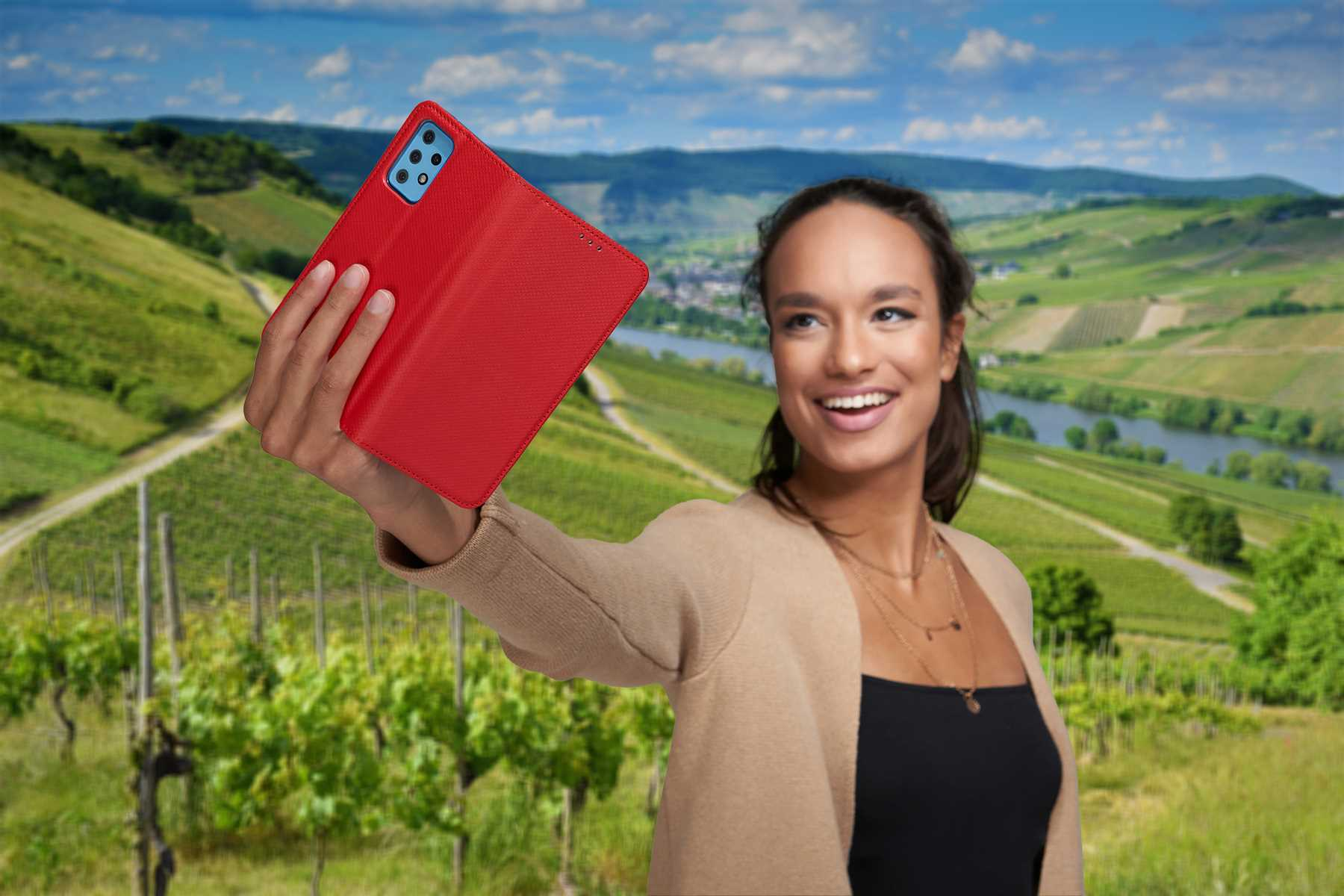 Frau hält rote Handyhülle, lächelt, mit malerischem Weinberg-Hintergrund.