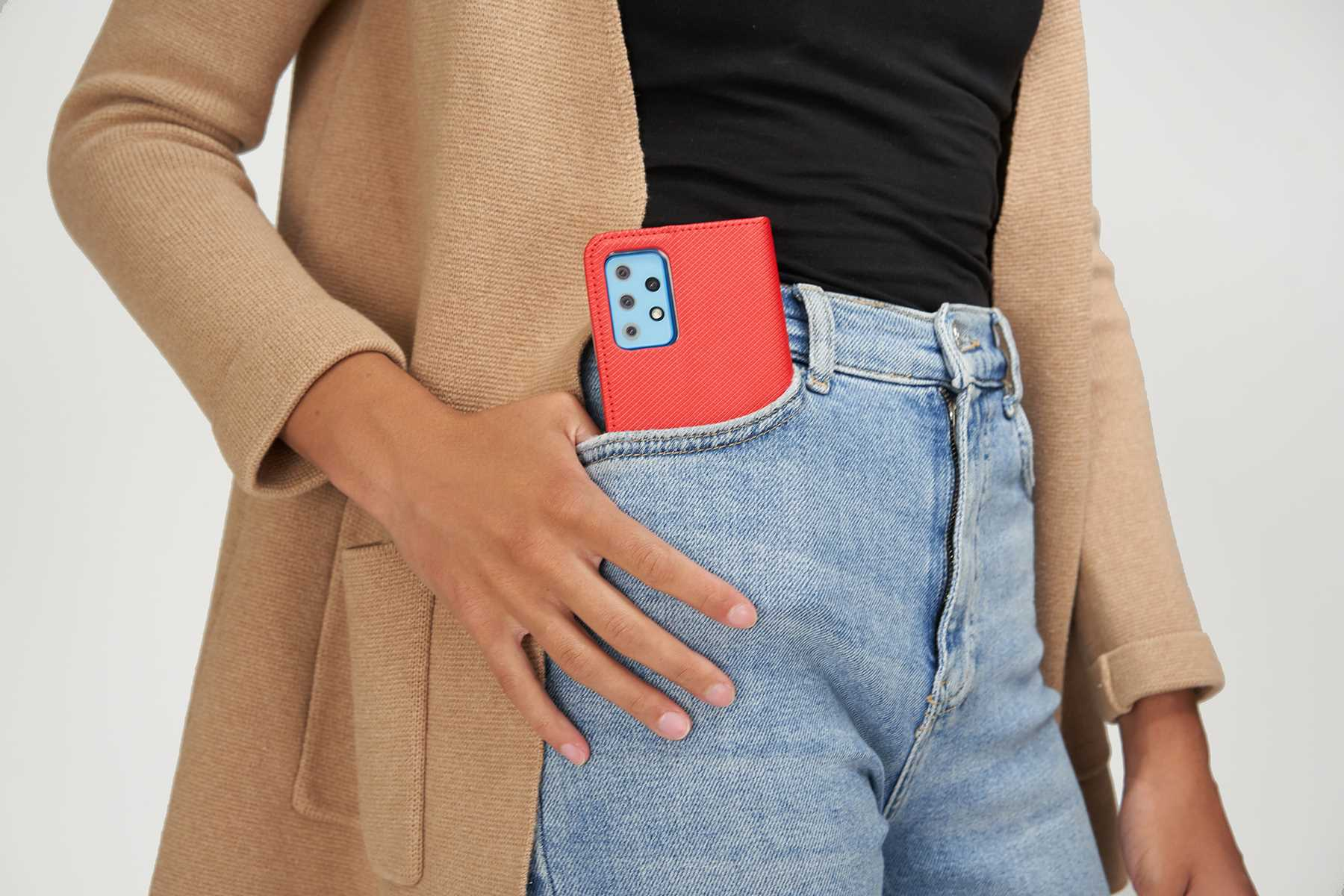 Eine Frau in Jeans und beigefarbenem Cardigan. Sie hält eine rote Handyhülle in ihrer Tasche.