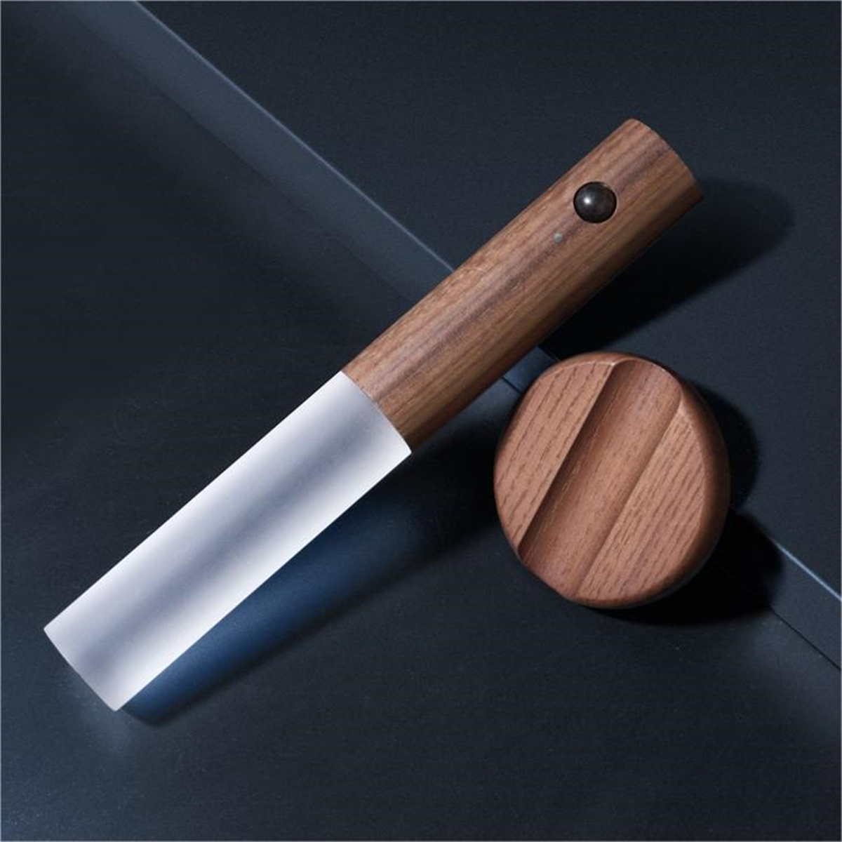 Ein Messer mit Holzgriff und mattierter Klinge neben einem runden Holzhalter.