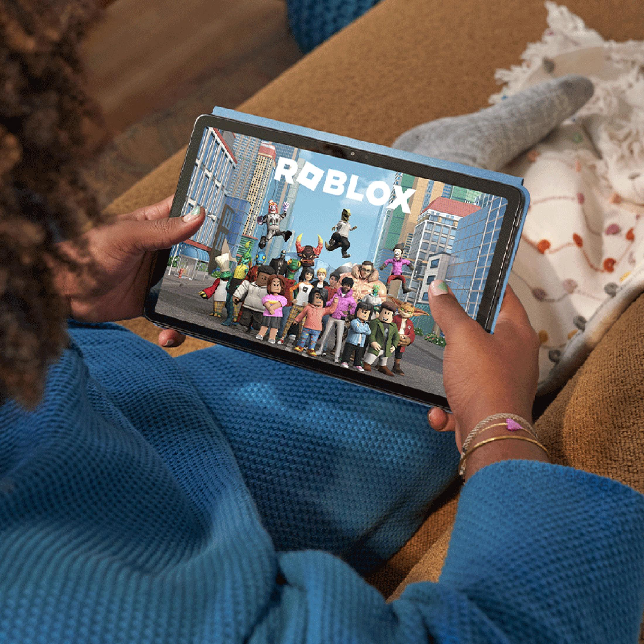Eine Person hält ein Tablet mit dem Roblox-Spiel auf dem Bildschirm. Die Person trägt ein blaues Hemd.