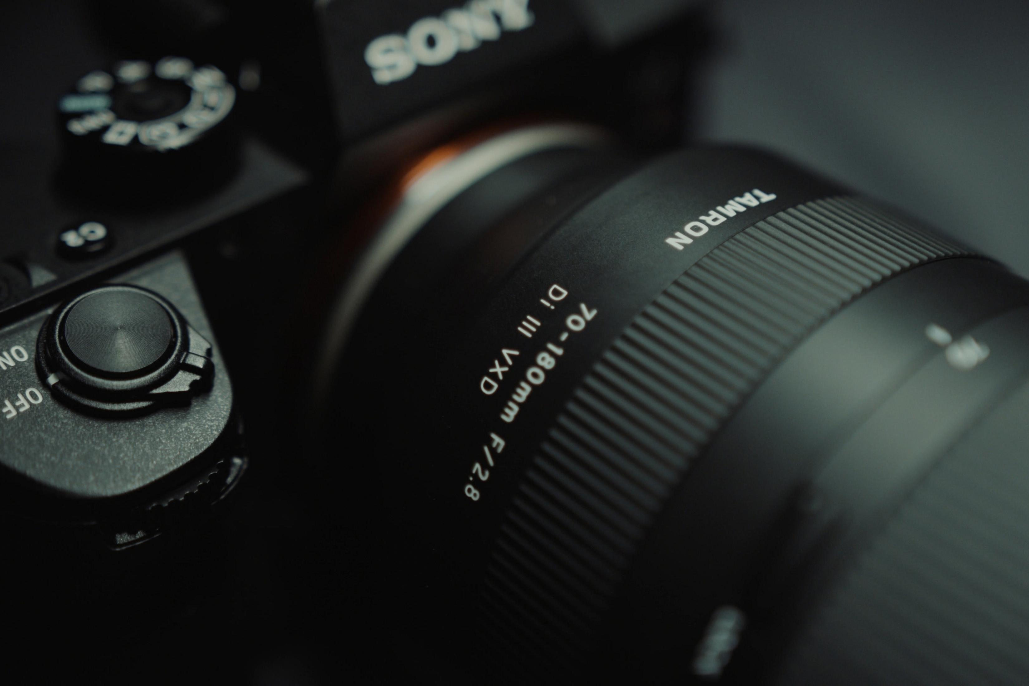 Czarny aparat z obiektywem Tamron. Obiektyw ma napis: 70-180mm Di III VXD f/2.8.