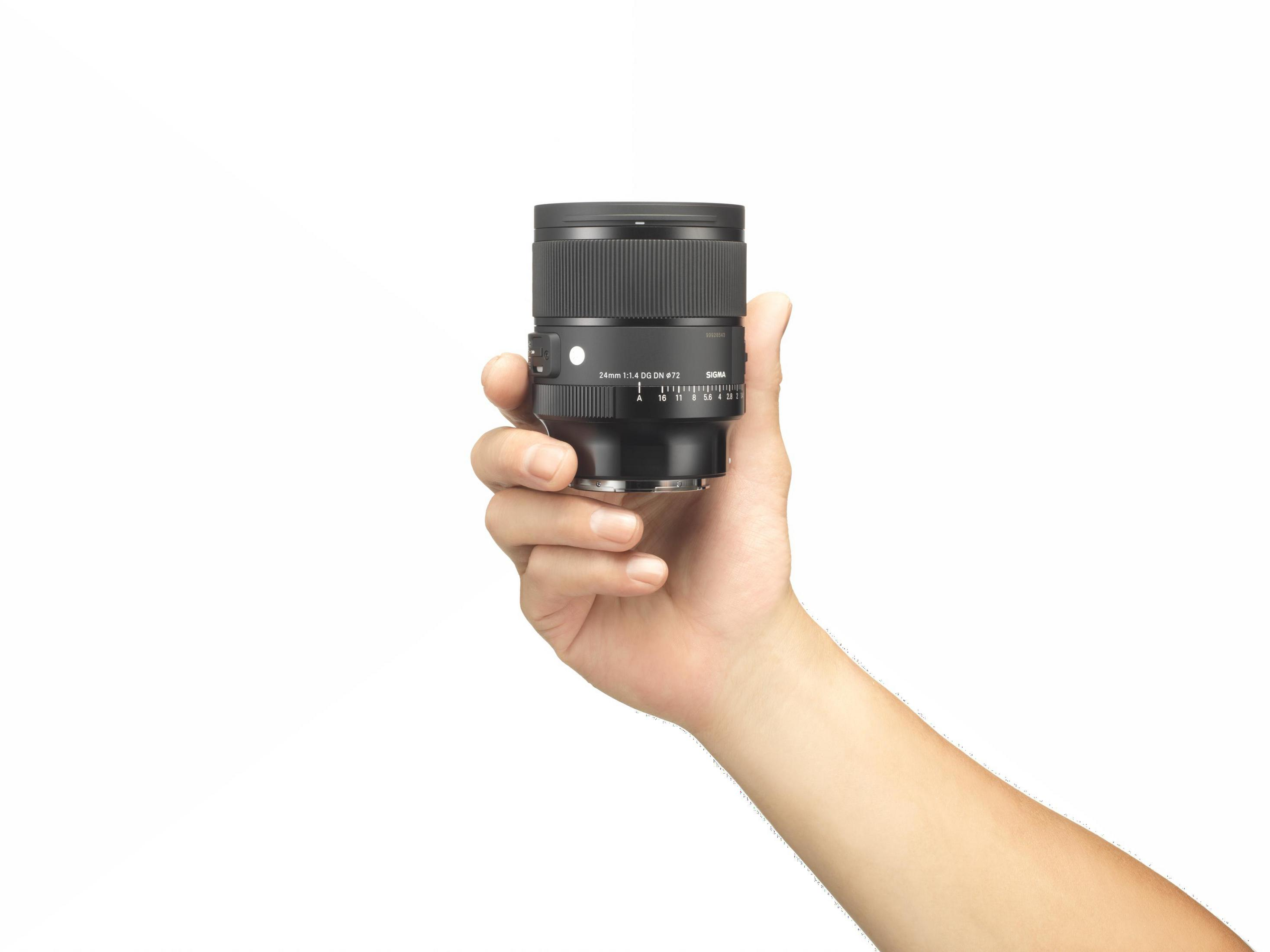 Ręka trzymająca czarny obiektyw aparatu. Obiektyw ma oznaczenia i pokrętło.