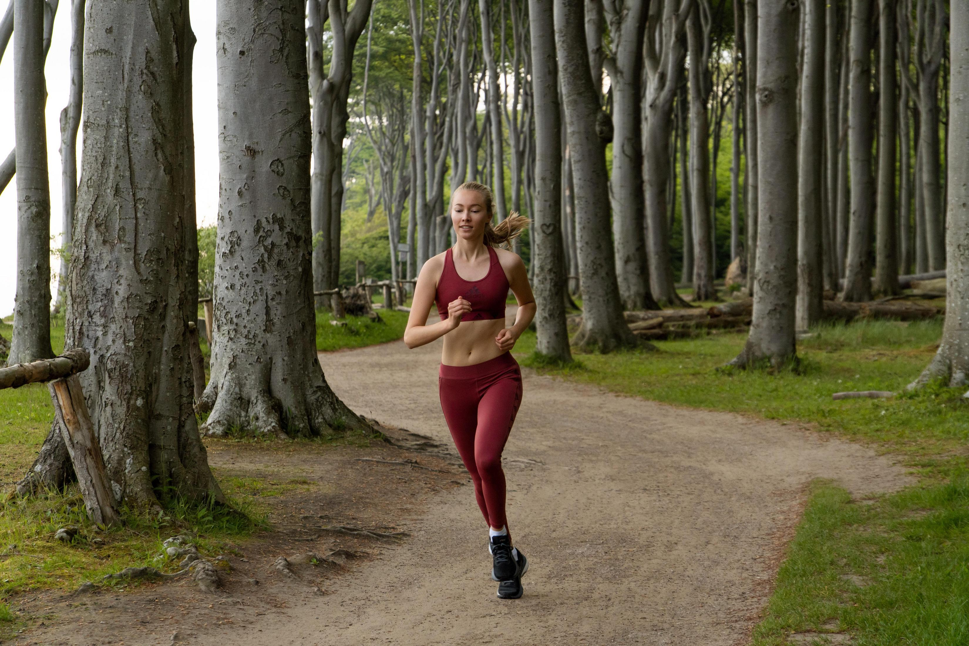 Kobieta biegnąca ścieżką przez las z wysokimi drzewami.