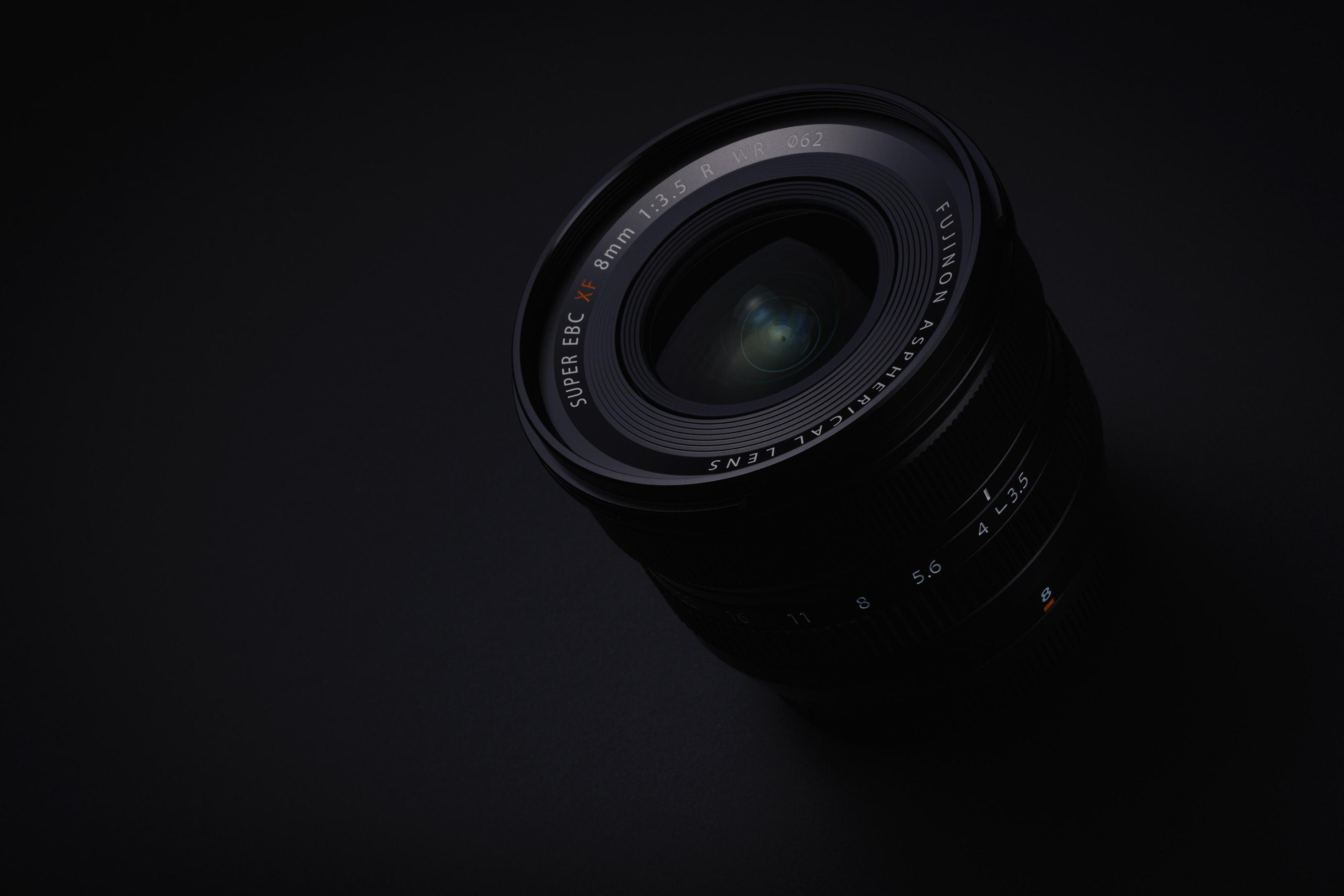 Czarny obiektyw z logo Fujinon na ciemnym tle, pokazujący elementy soczewek.