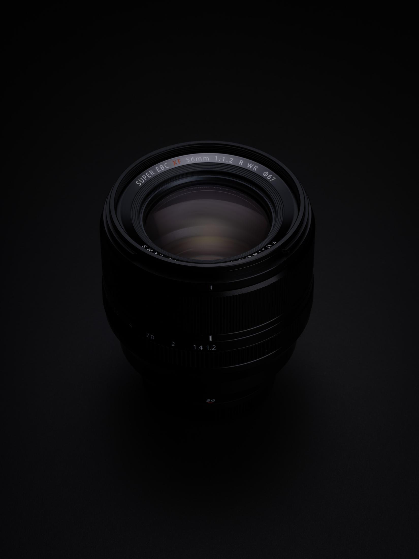 Czarny obiektyw aparatu, widok z boku. Obiektyw jest ciemny, w czarnym otoczeniu.