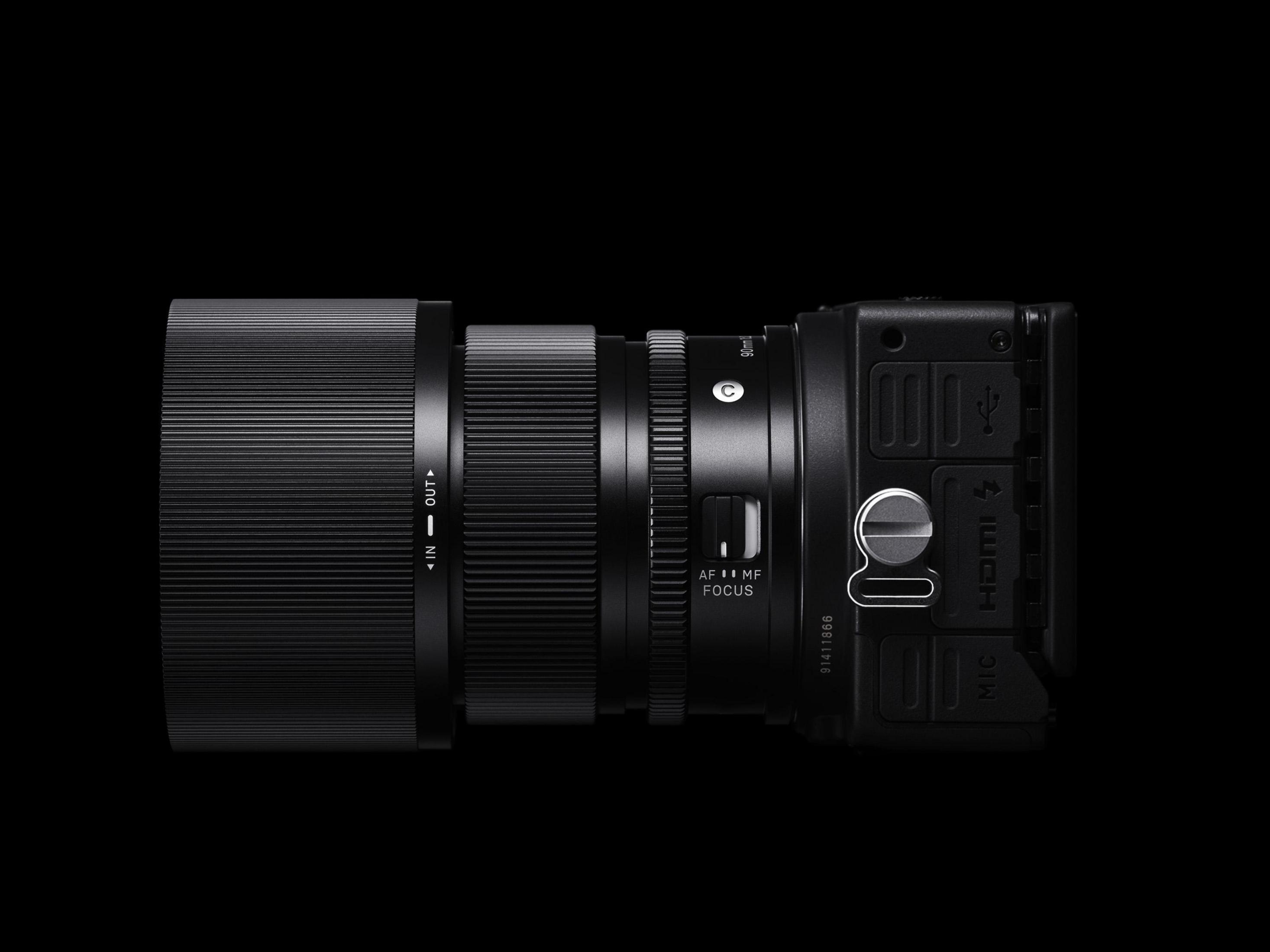 Czarny aparat z długim obiektywem na czarnym tle. Widok z boku.