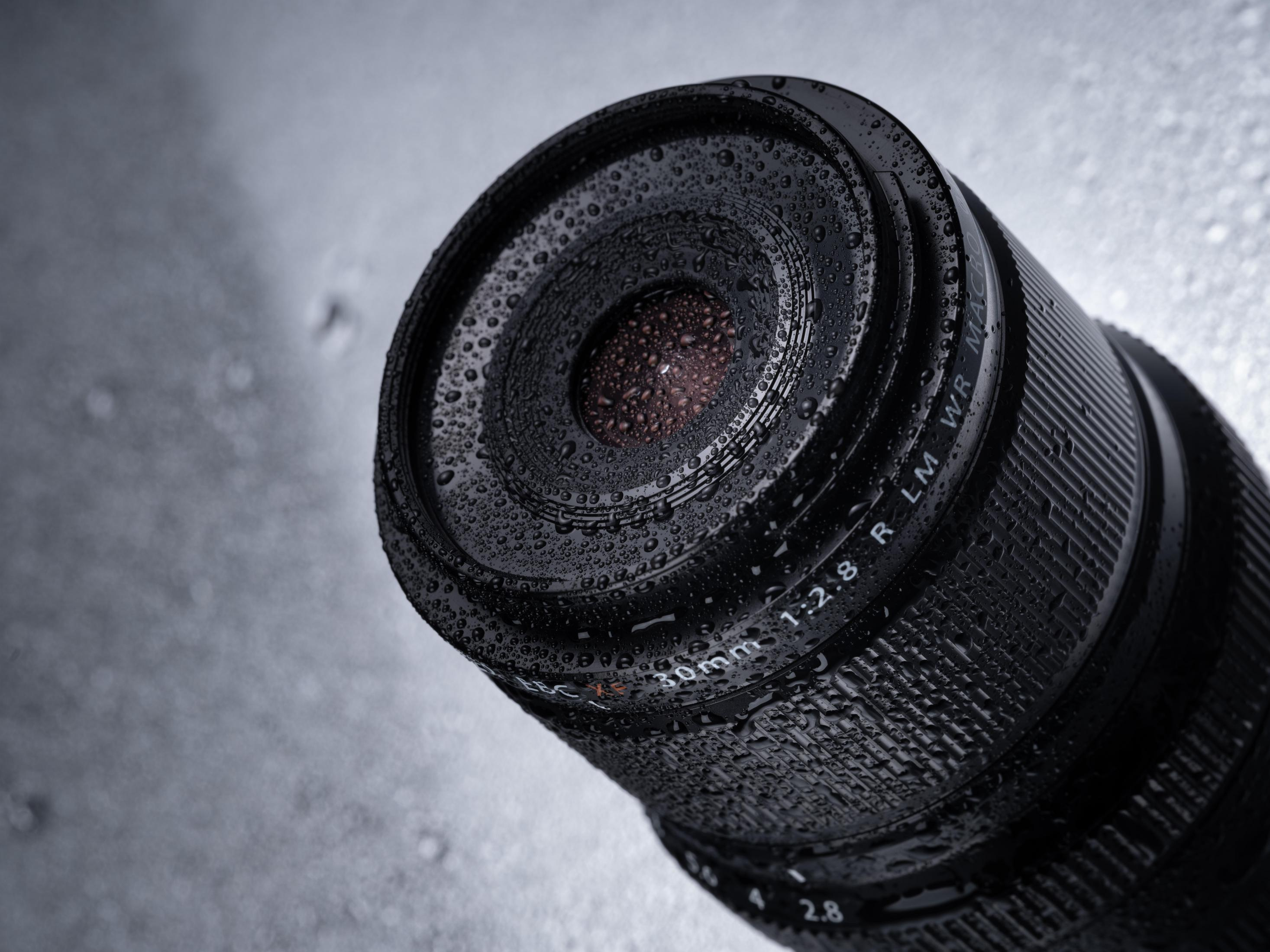 Czarny obiektyw aparatu z kroplami wody, z rozmytym tłem.
