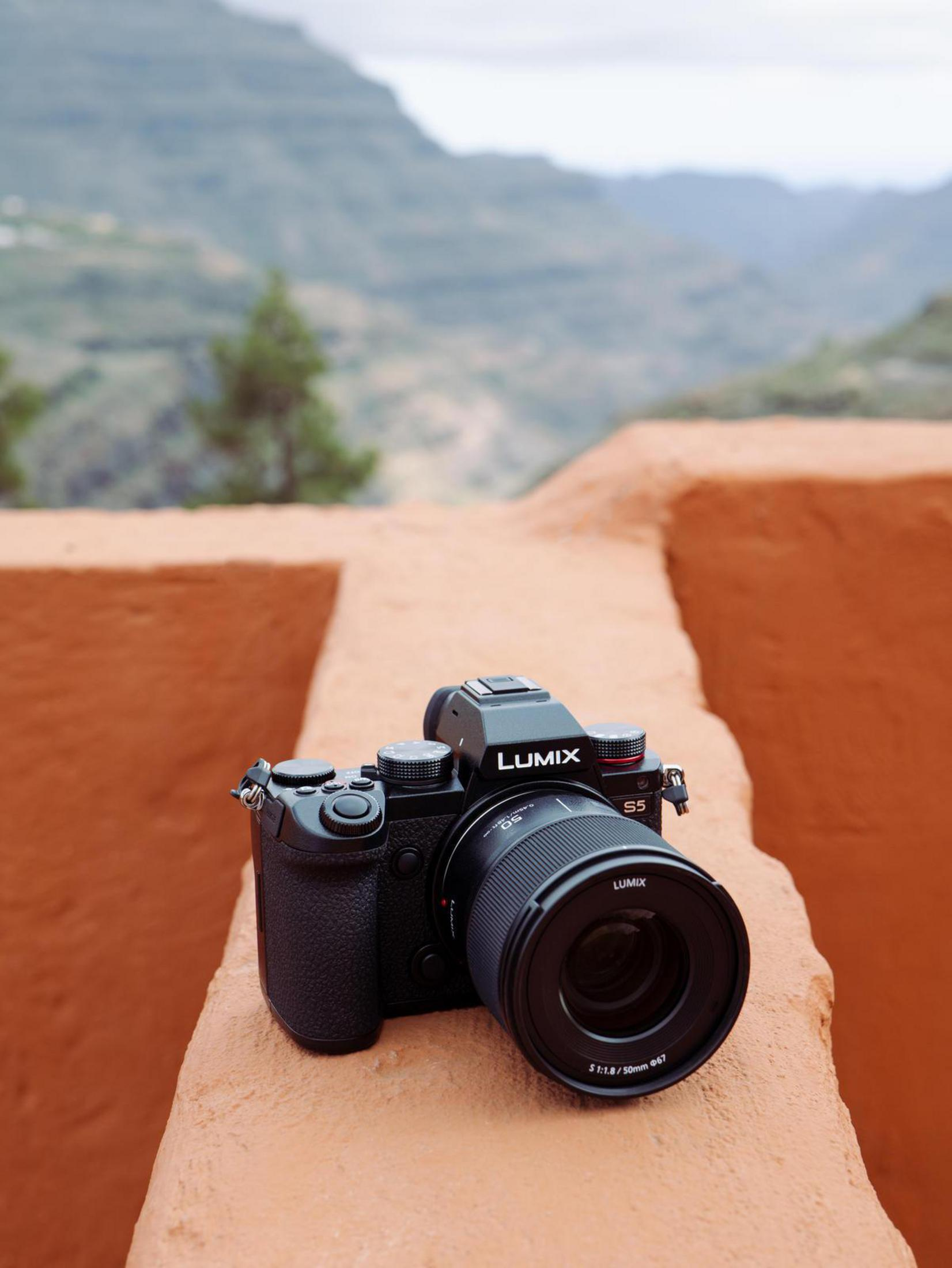 Eine schwarze Lumix-Kamera steht auf einer Mauer, im Hintergrund eine Berglandschaft.