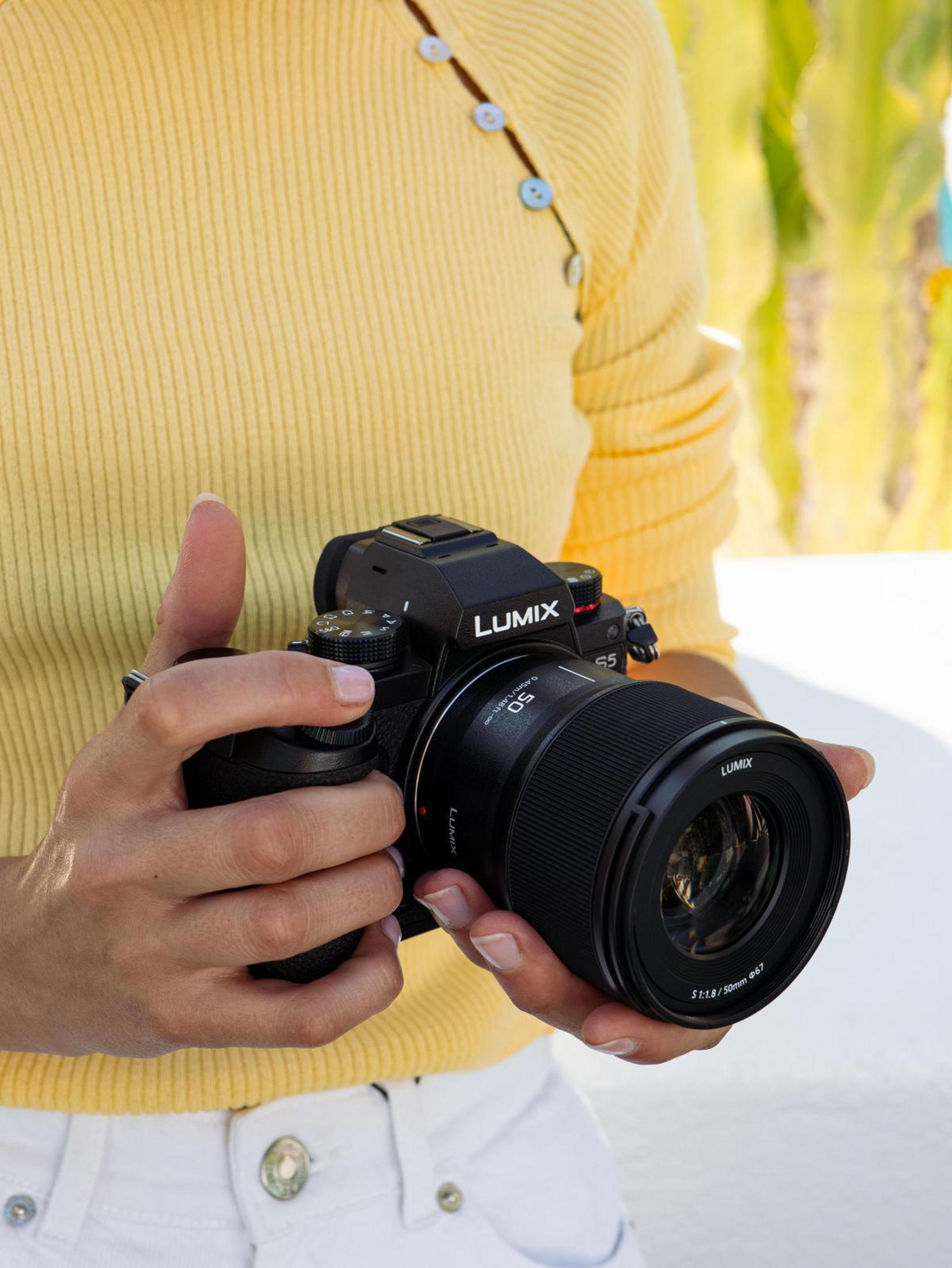 Person hält eine schwarze Lumix-Kamera mit Objektiv.