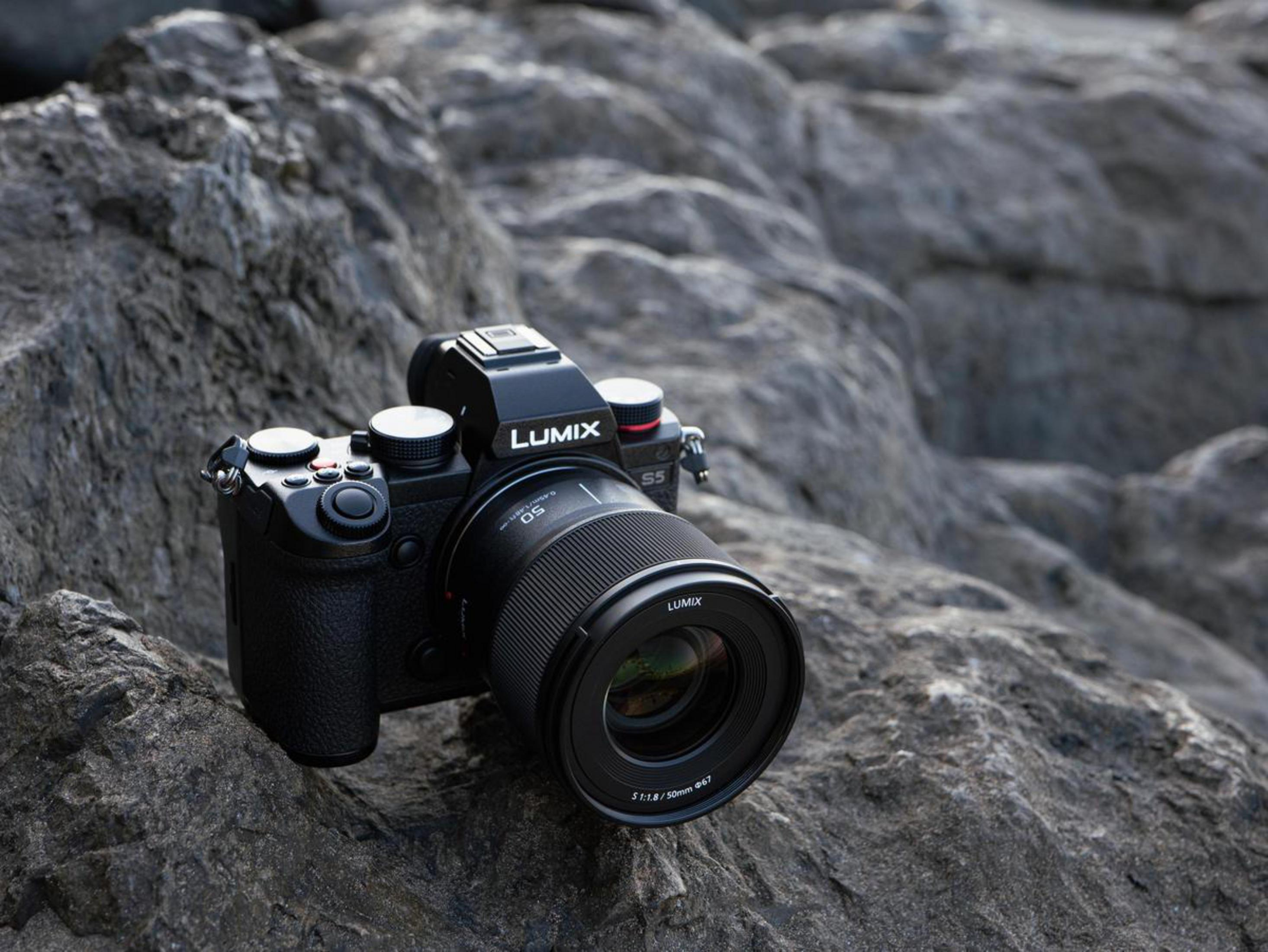 Eine schwarze Lumix-Kamera mit Objektiv, die auf einer felsigen Oberfläche im Freien liegt.
