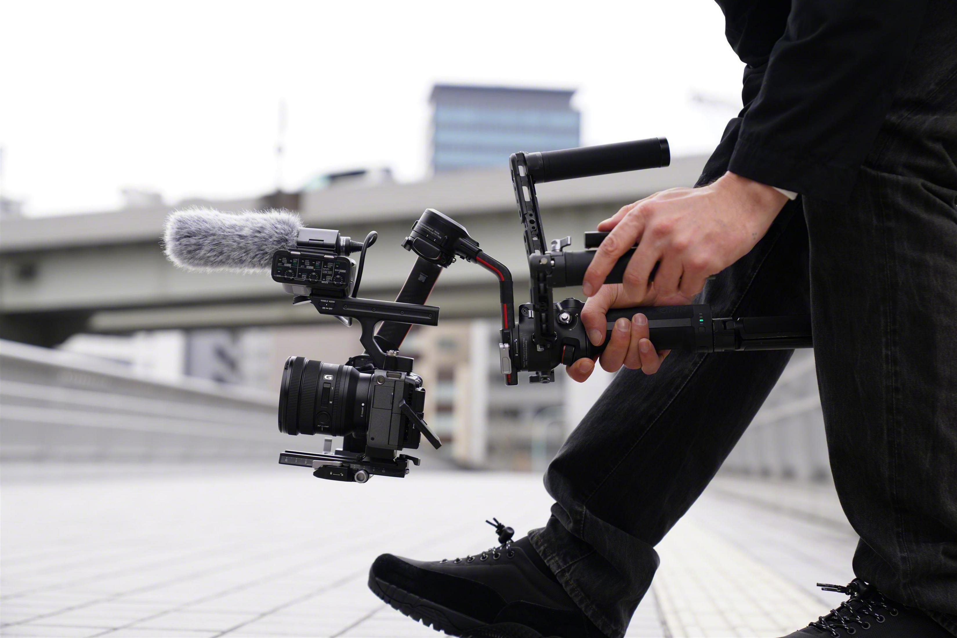 Osoba trzymająca zestaw kamer, filmująca na zewnątrz. Kamera jest zamontowana z mikrofonem.