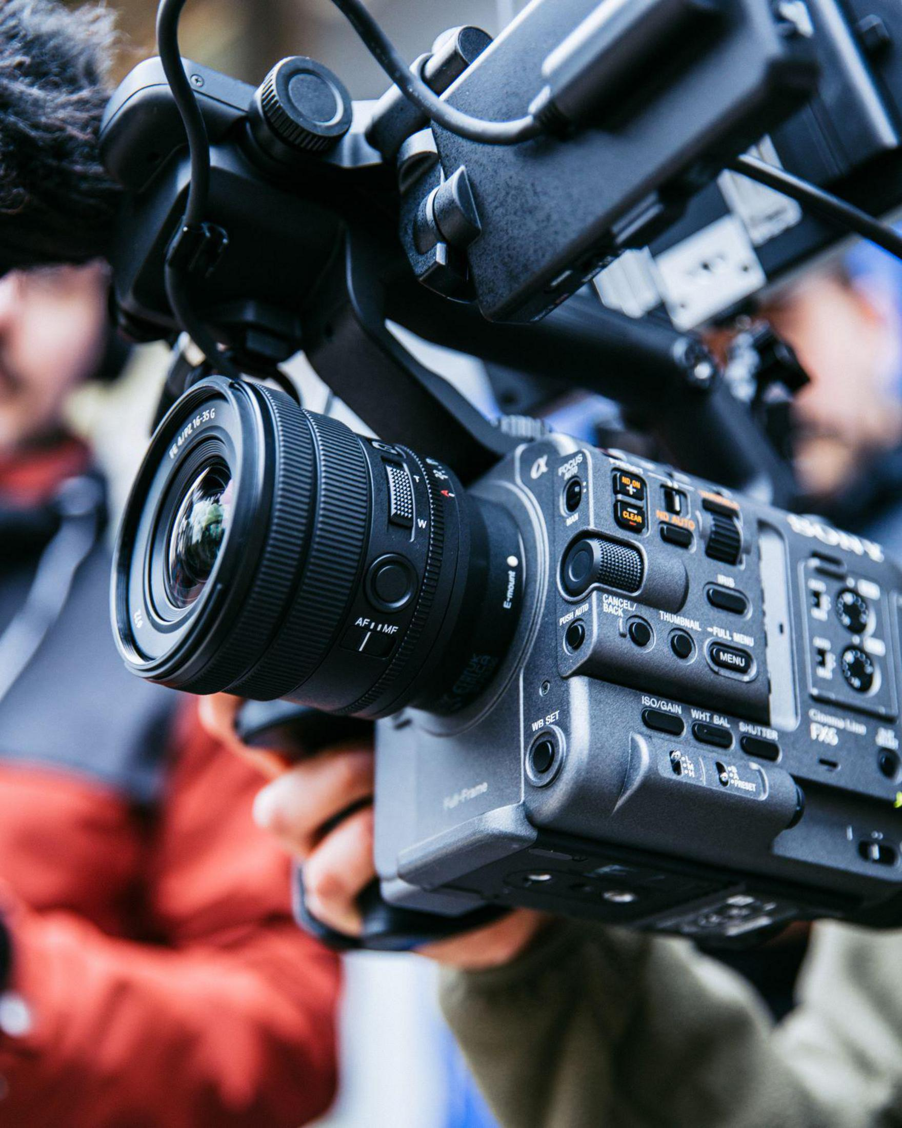 Zbliżenie aparatu z obiektywem trzymanym przez osobę, z rozmytym tłem.