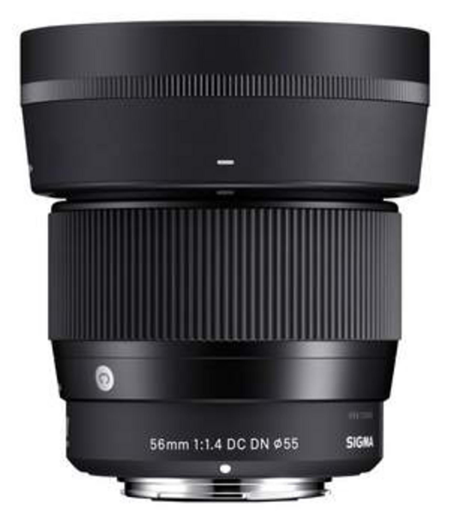 Czarny obiektyw Sigma 56mm. Obiektyw posiada rowkowany pierścień ostrości. Tło jest białe.
