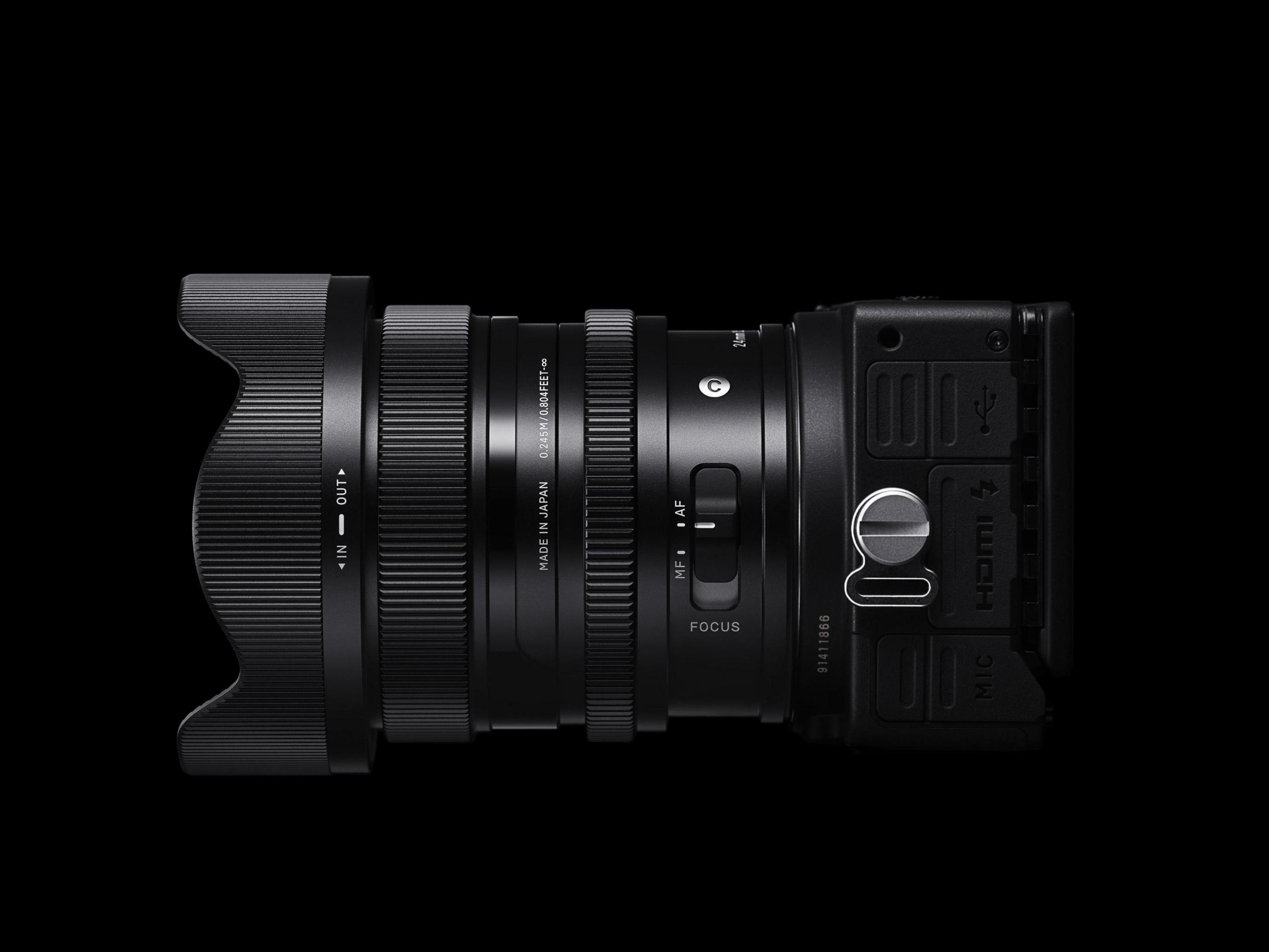 Czarny obiektyw z osłoną przeciwsłoneczną przymocowaną do czarnego korpusu aparatu, na czarnym tle.