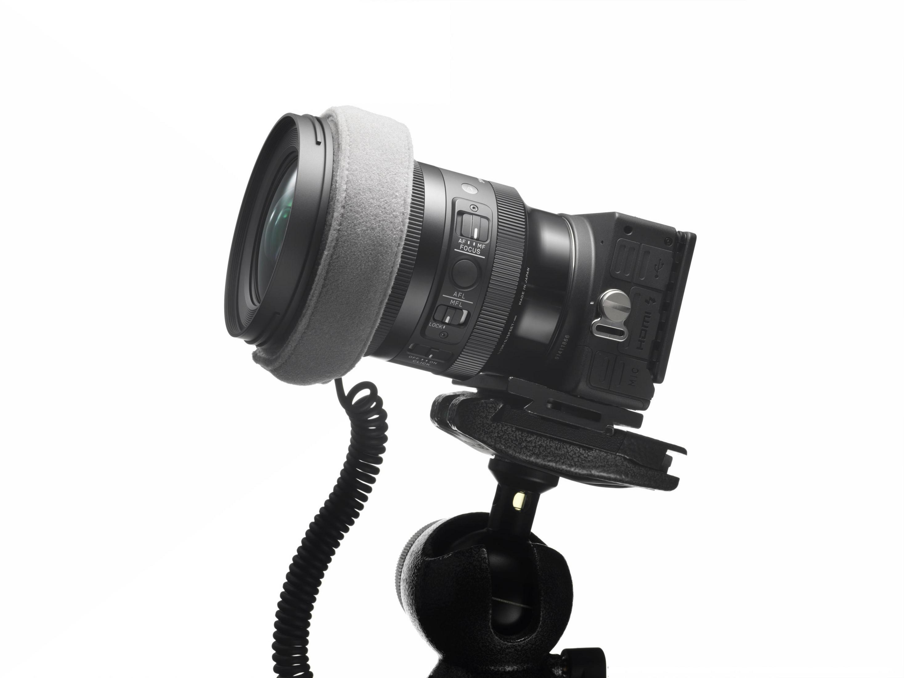 Aparat zamontowany na statywie z obiektywem i dyfuzorem światła. Obiektyw skierowany w stronę widza, tło jest białe.