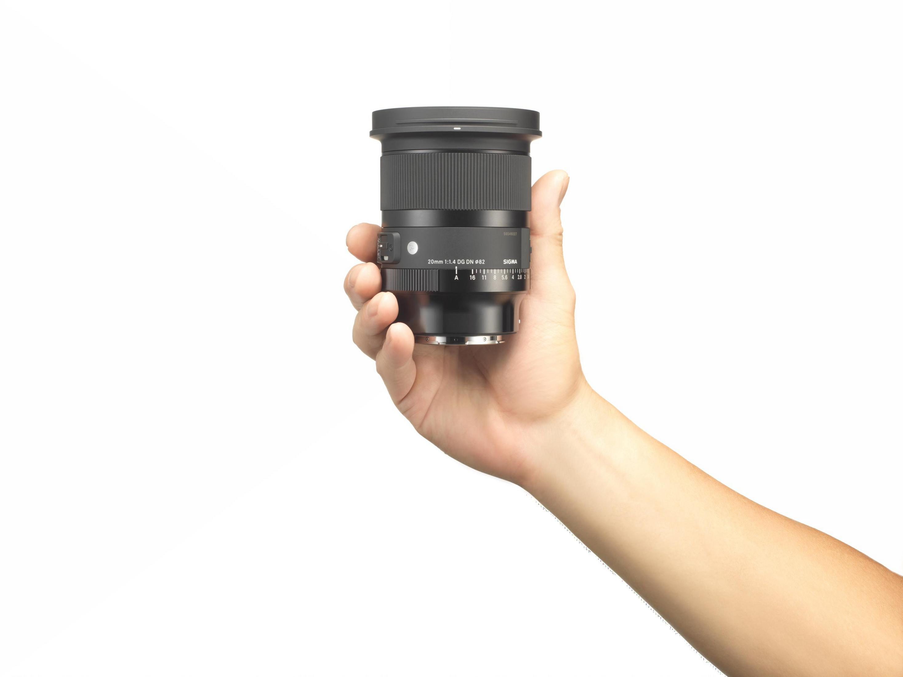Ręka trzyma czarny obiektyw aparatu. Obiektyw posiada pierścień ostrości i oznaczenia.
