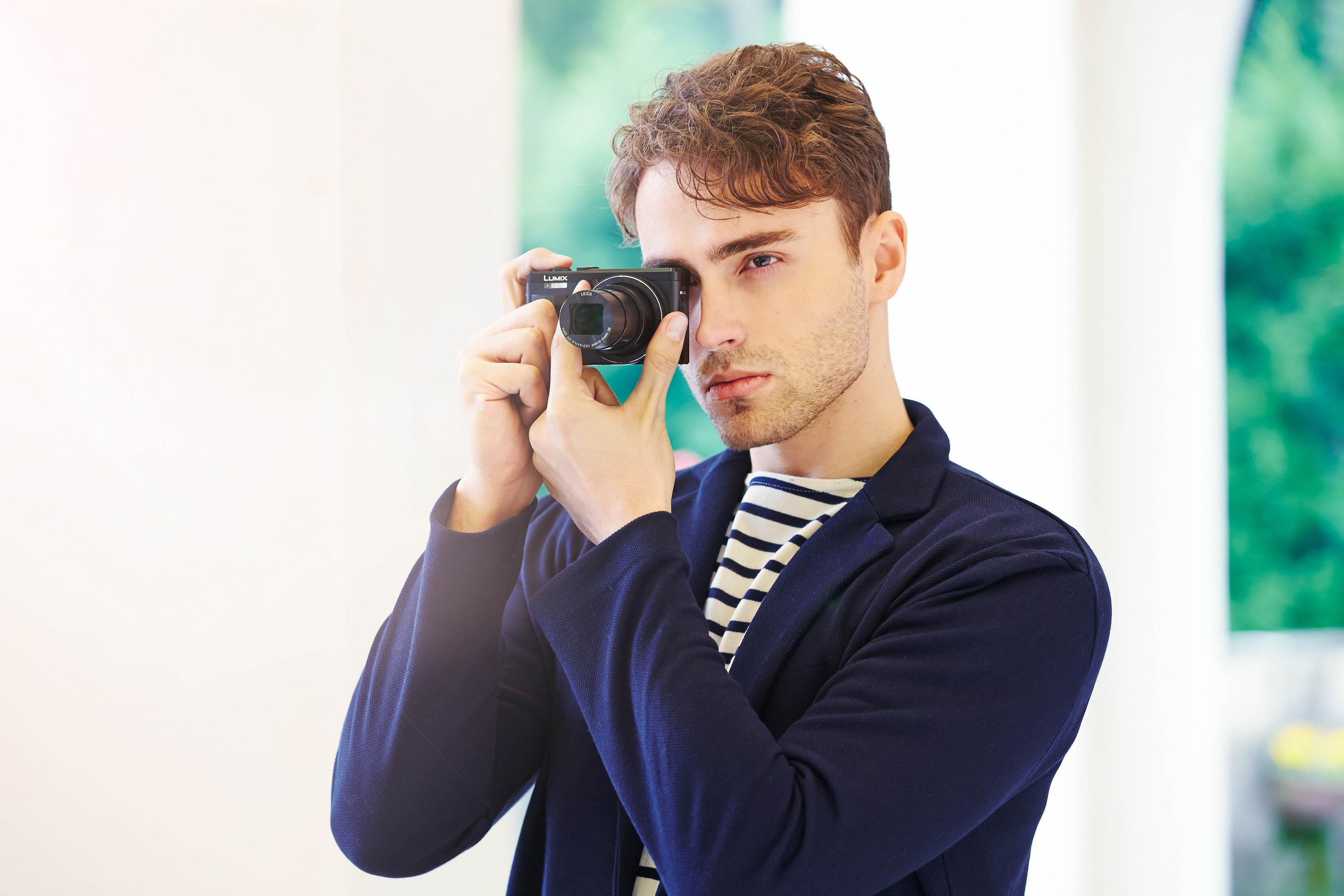 Ein Mann, der mit einer schwarzen Kamera fotografiert, trägt ein gestreiftes Hemd und eine blaue Jacke.
