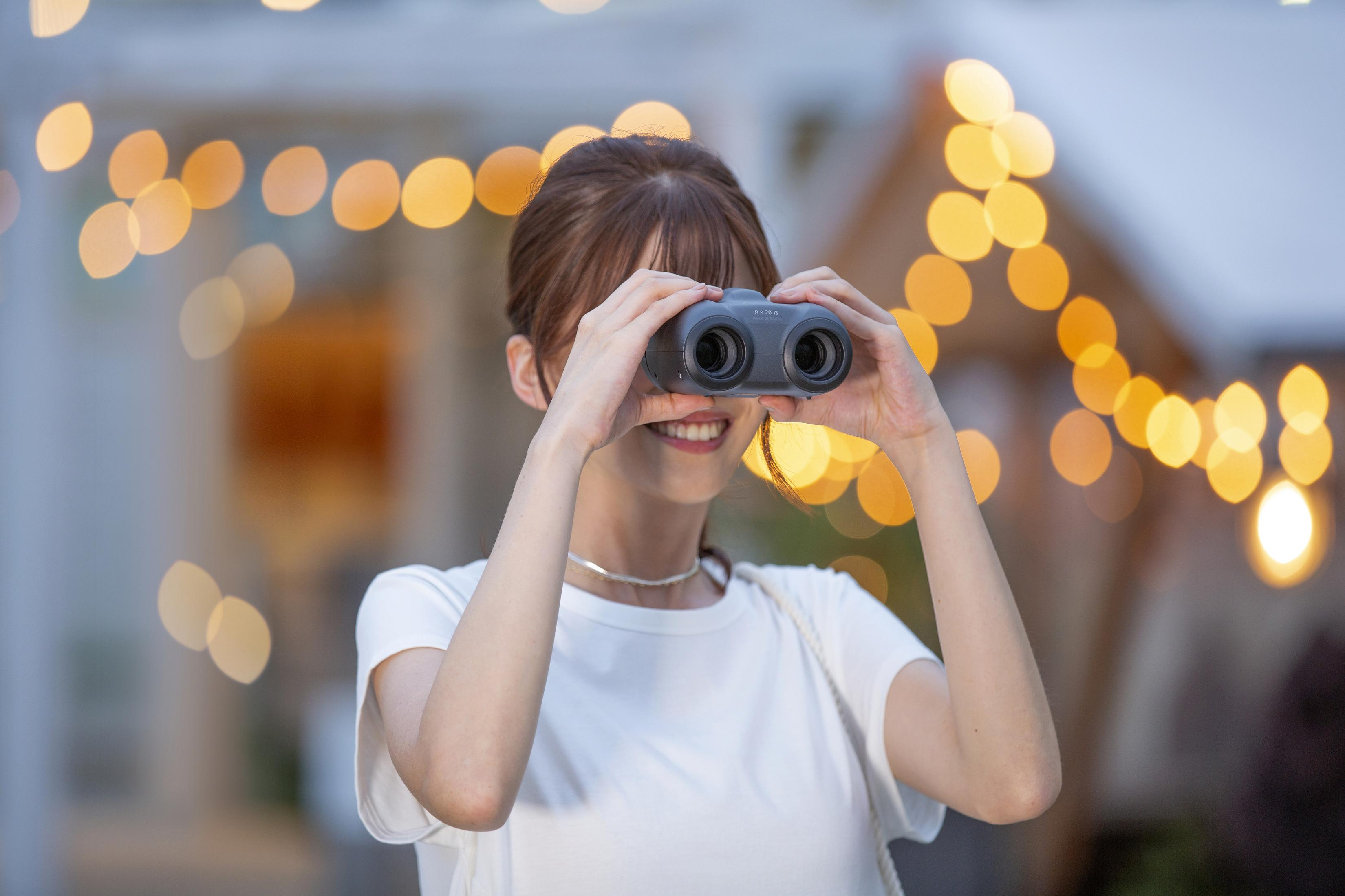 Kobieta uśmiecha się, patrząc przez lornetkę. Tło z światłami.