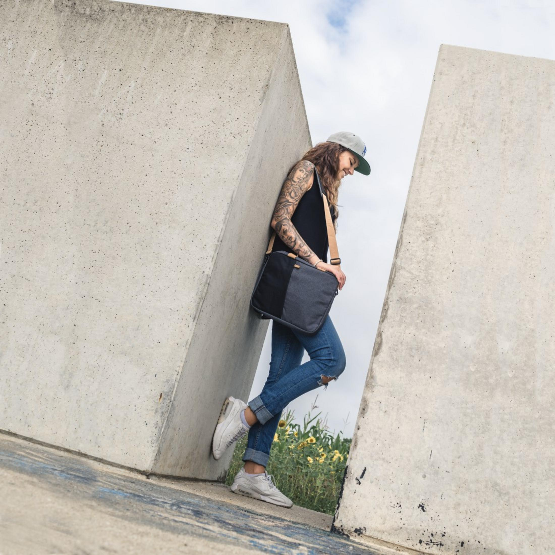 Donna appoggiata a muri di cemento con borsa nera e jeans.