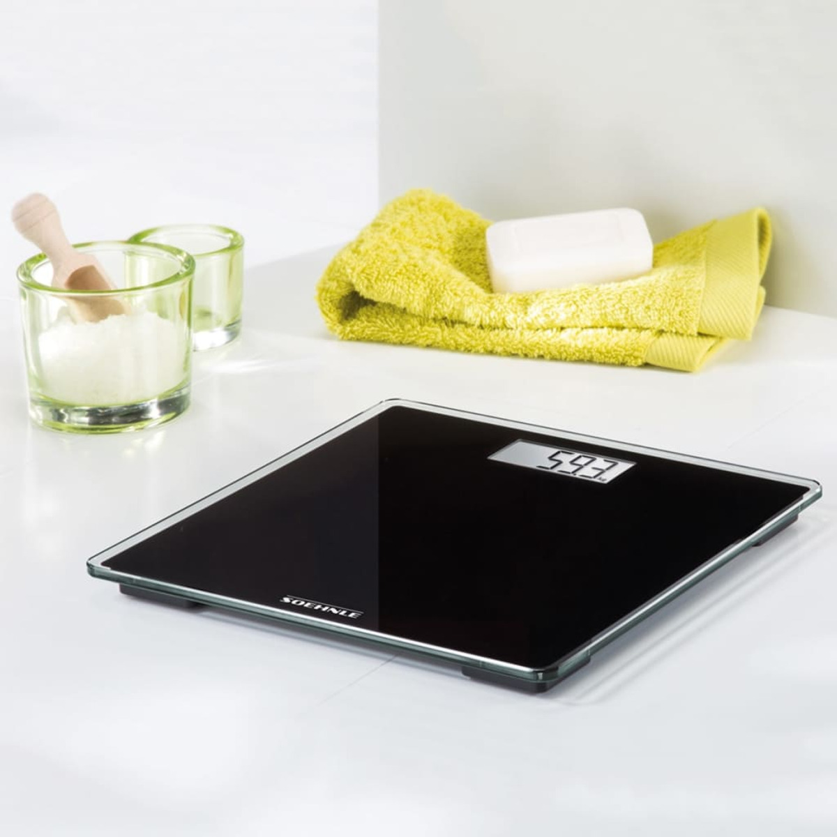 Eine schwarze Digitalwaage mit Gewichtsanzeige, mit Seife, Handtuch und Zubehör.