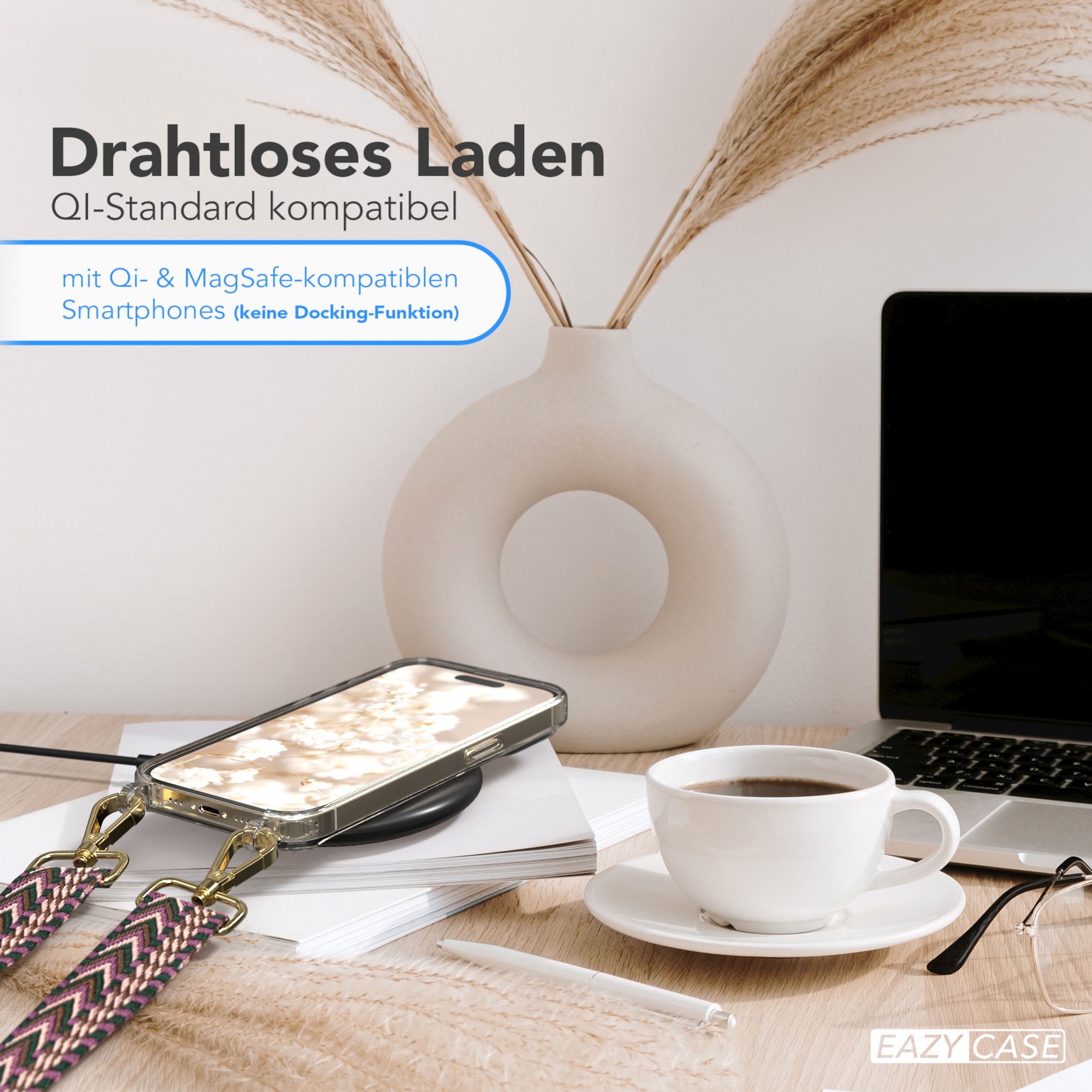 Telefon mit Band auf kabellosem Ladegerät, neben Kaffeetasse, Stift und Vase mit Trockenpflanzen.