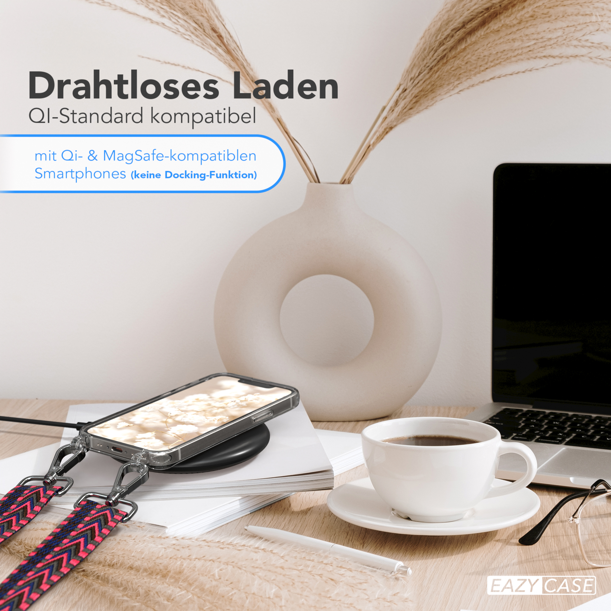 Telefon mit Gurt, der auf einem Pad geladen wird, Vase und Tasse auf dem Tisch. Laptop im Hintergrund.