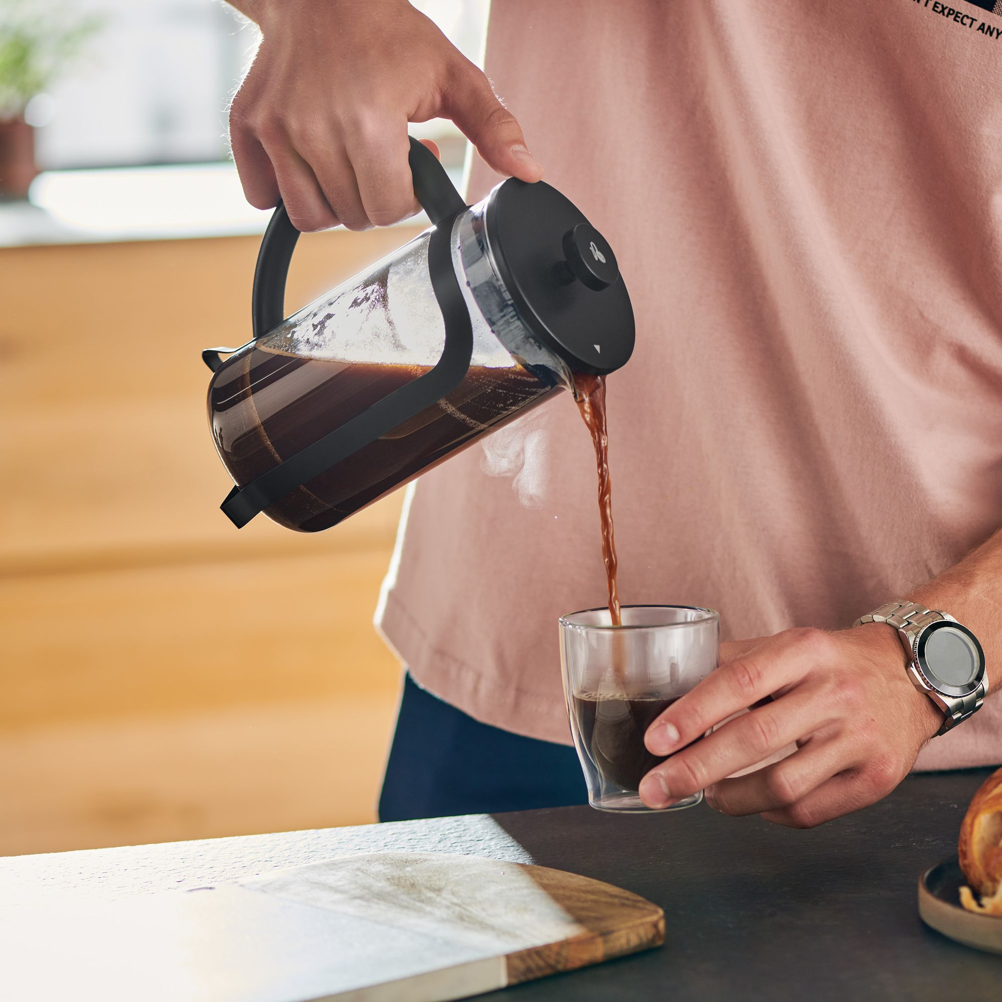 Eine Person gießt Kaffee aus einer French Press in ein Glas.