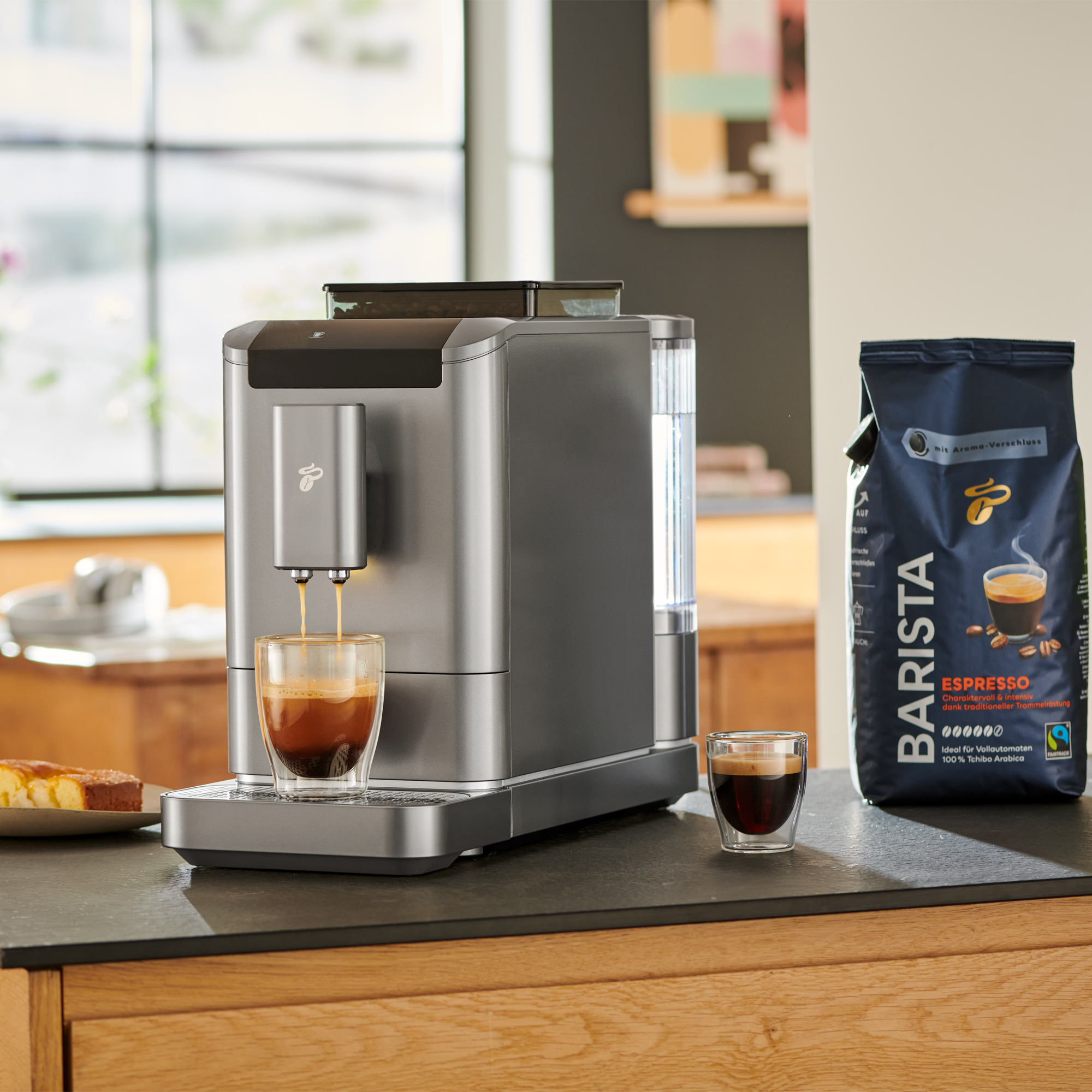 Espressomaschine, die Kaffee in ein Glas brüht, mit einer Kaffeebohnentüte und Kuchen.